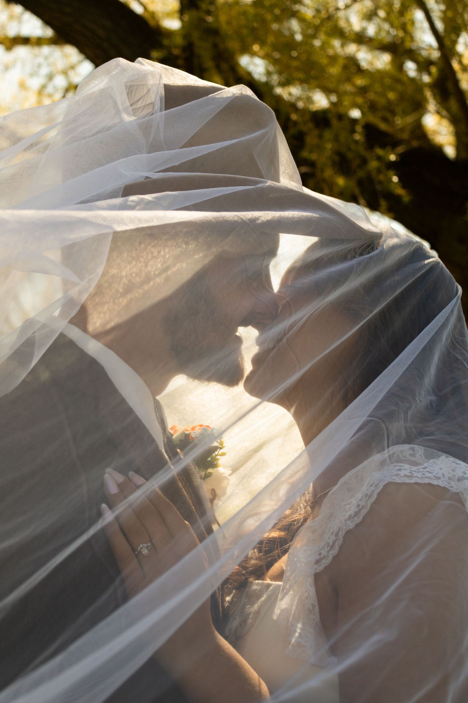 Bride and Groom pose under veil at golden hour