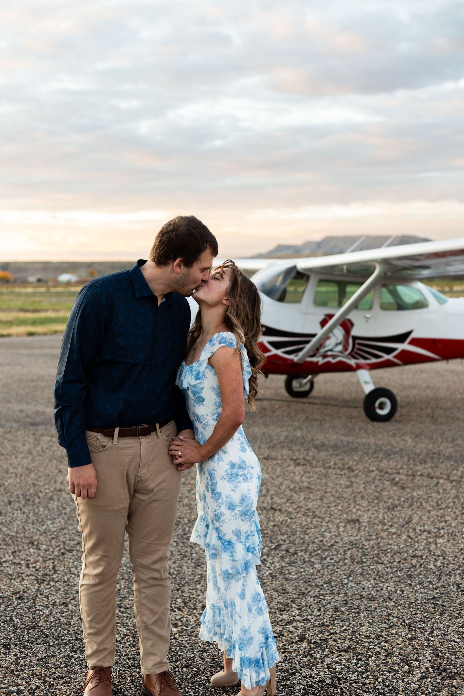 man kisses fiance in front of small airplane