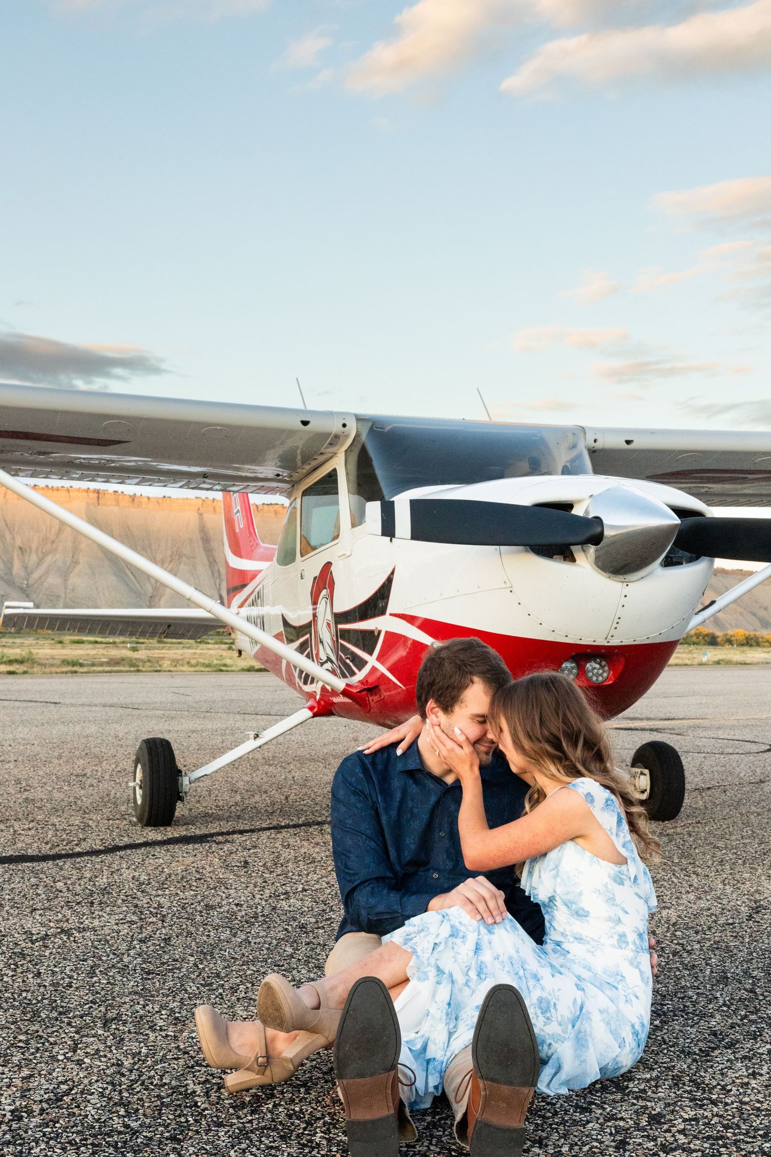 couple sits on runway in front of small airplane