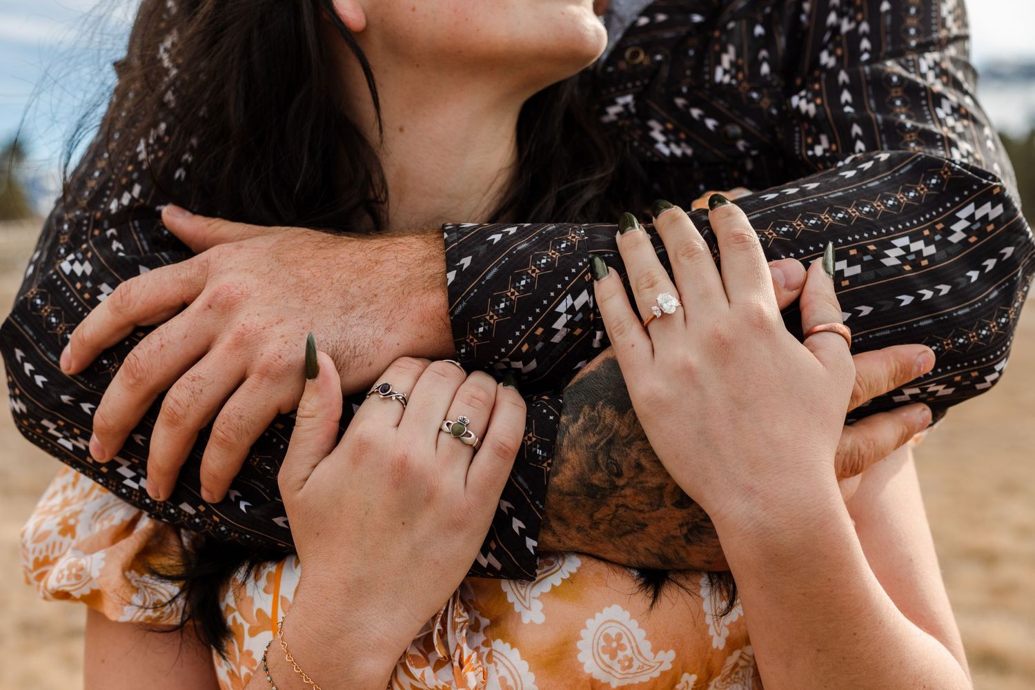 man hugs fiance from behind showing off ring