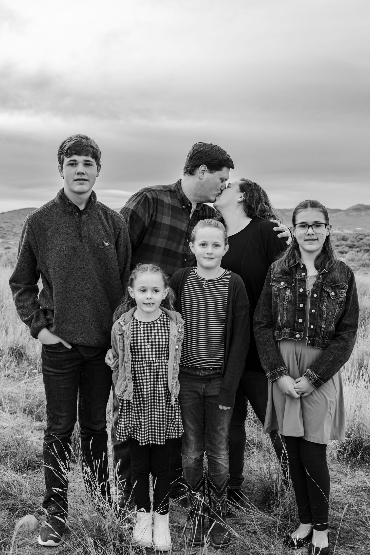 mom and dad kiss while kids look at camera