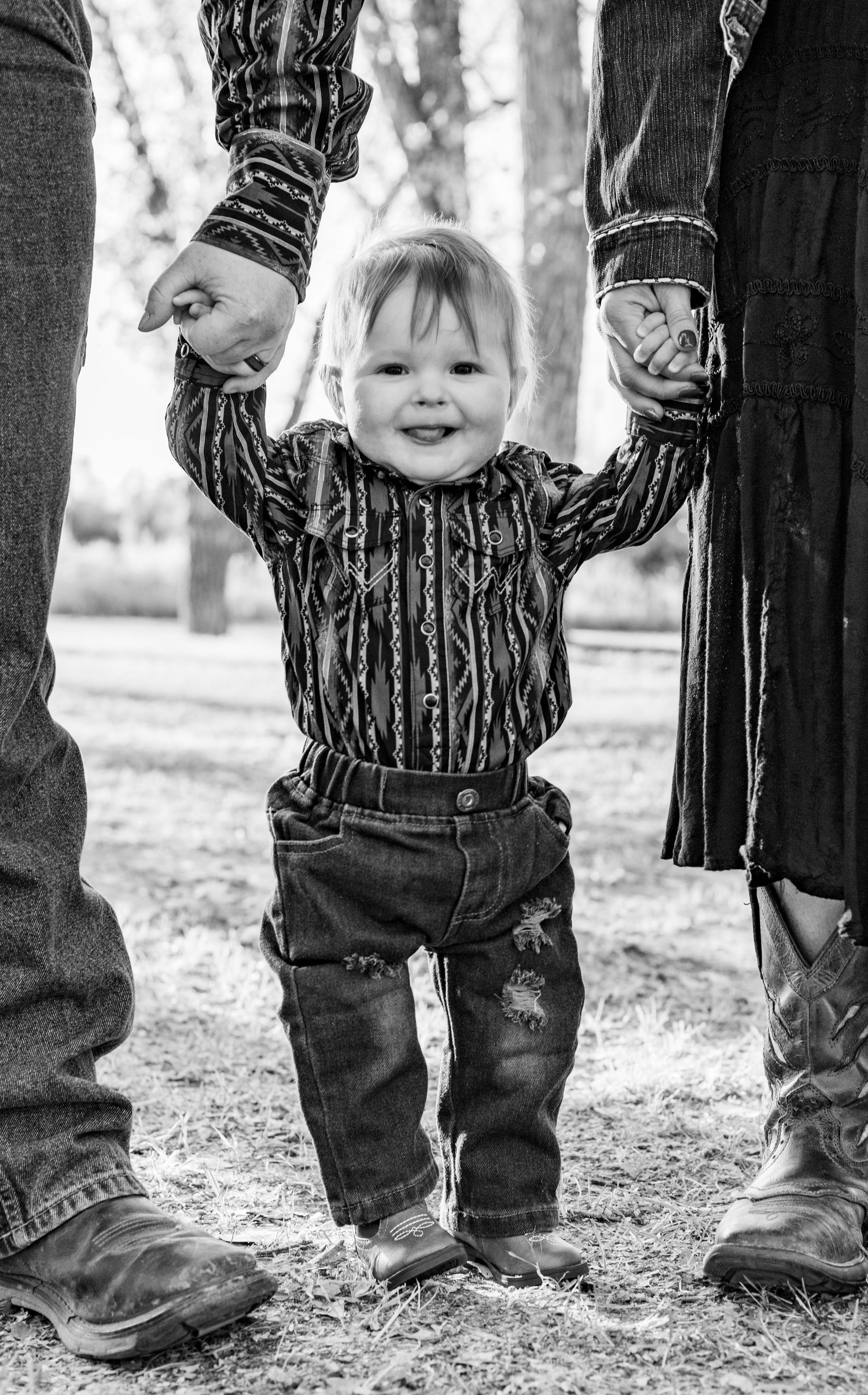 baby stands holding mom and dads hands