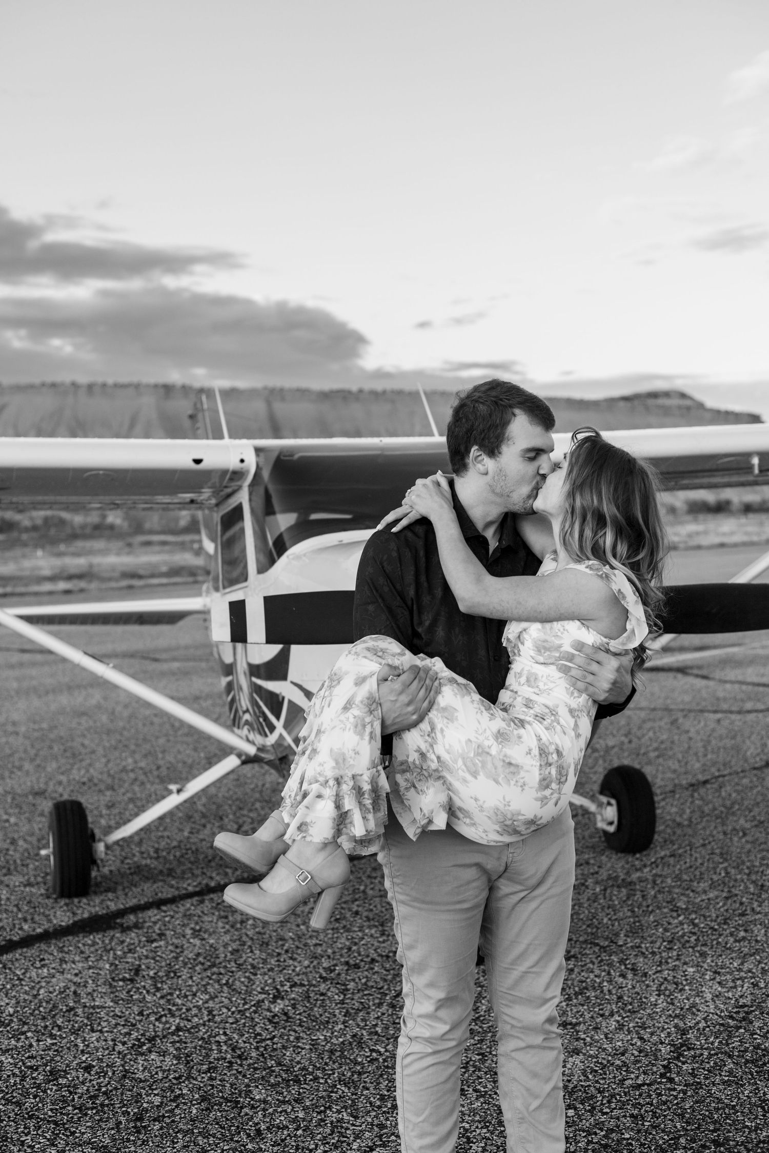 man lifts fiance and kisses her in front of small airplane