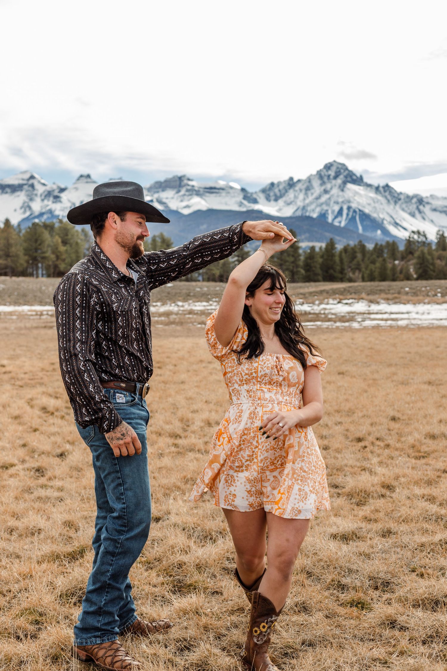man spins fiance in front of mountain background