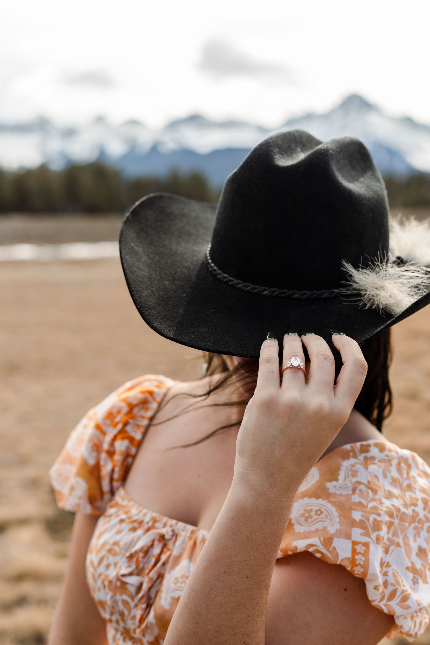woman wears cowboy hat and grab the rim showing off engagement ring