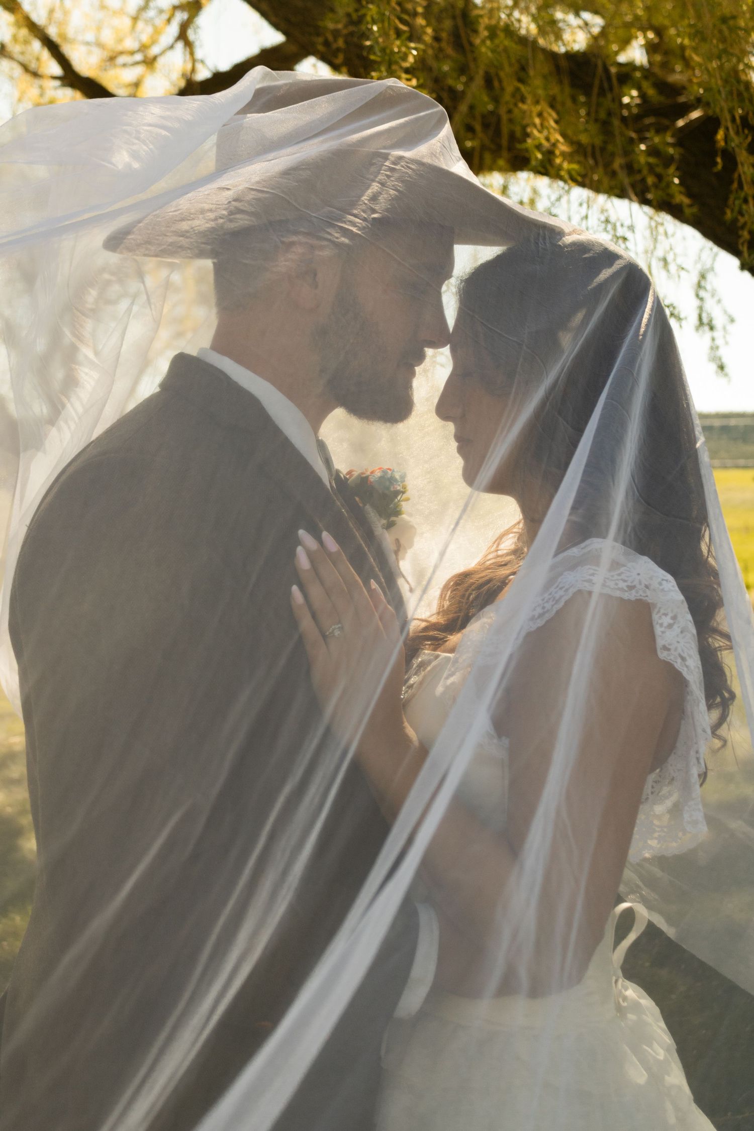 Bride and Groom pose under veil at golden hour