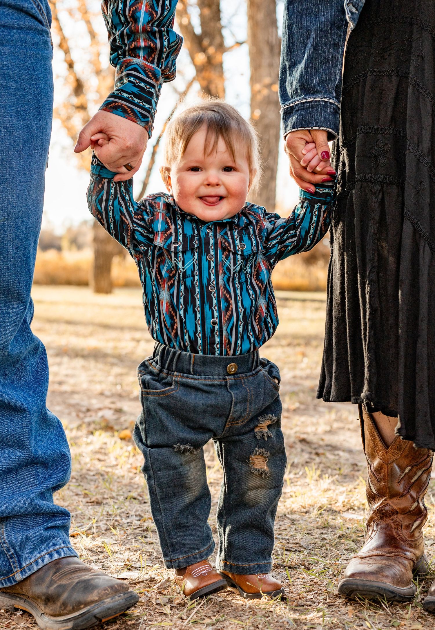 baby stands holding mom and dads hands