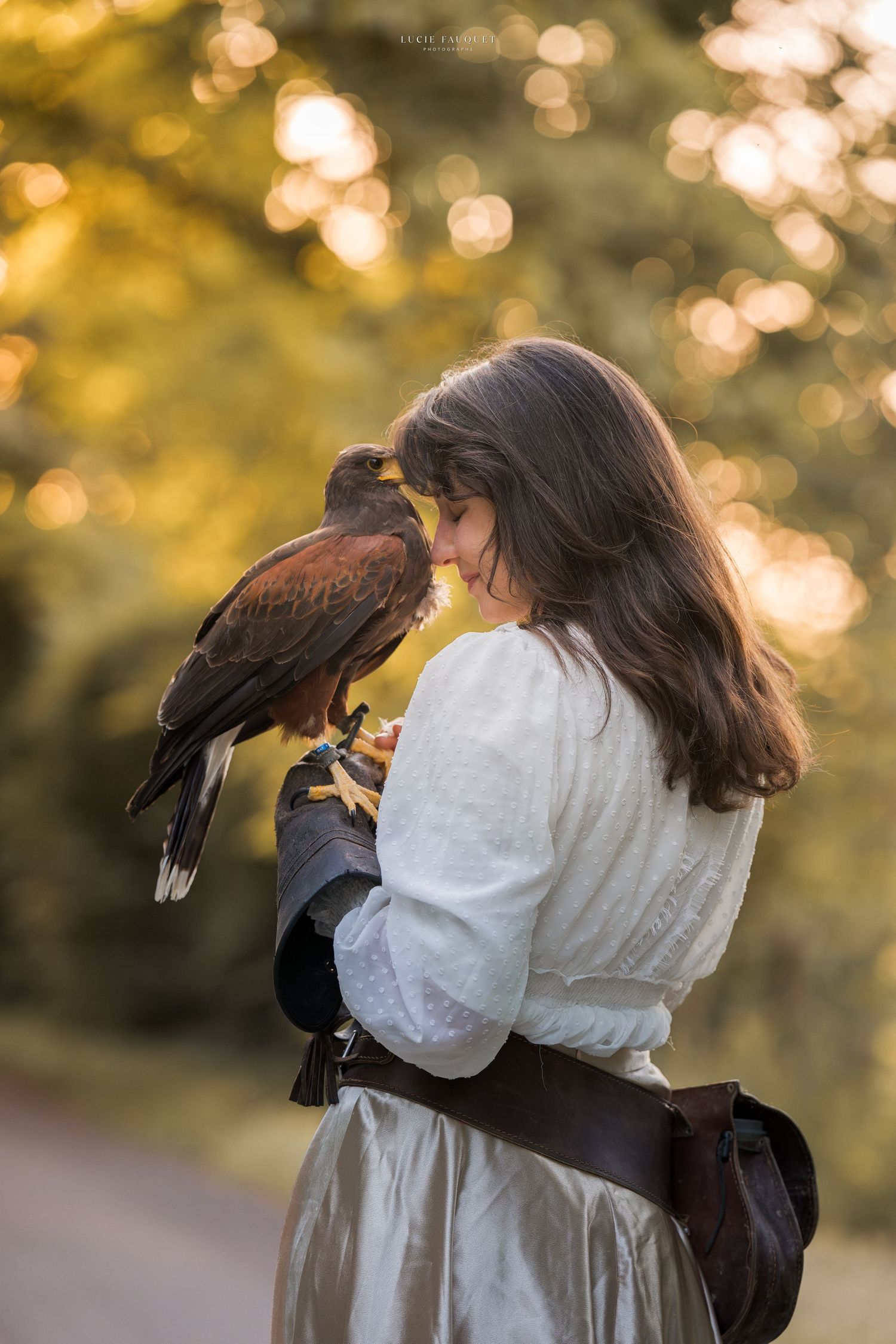Woman in medieval dress holding a Harris hawk on her gloved hand in golden hour light outdoors.