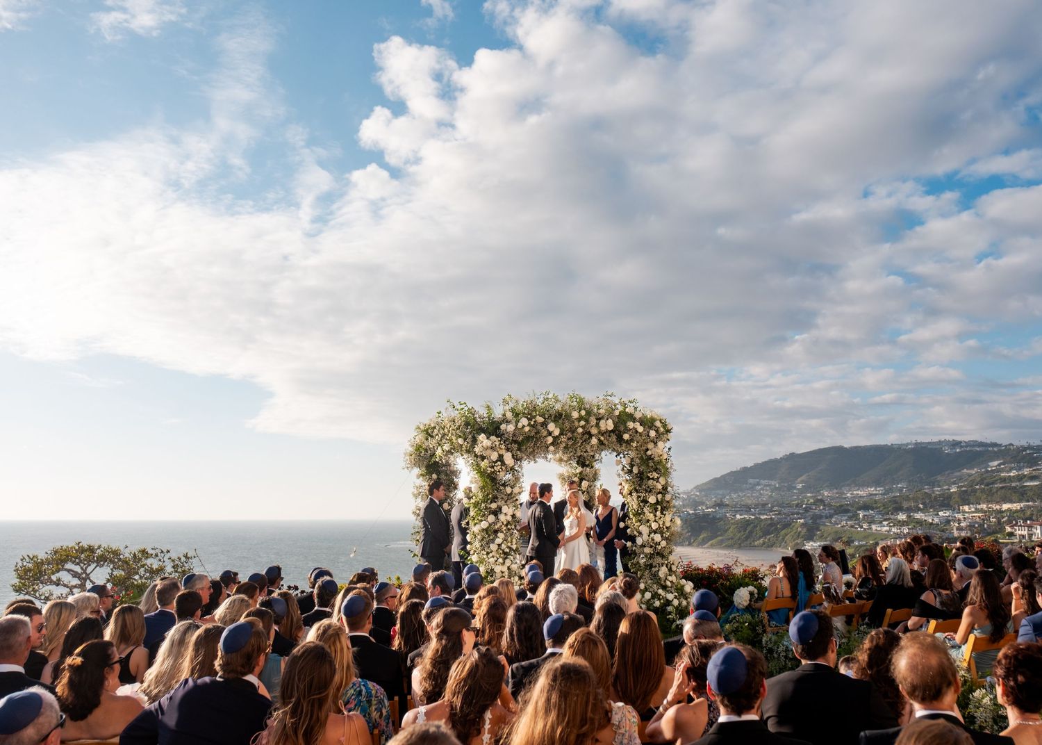 Outdoor Jewish wedding ceremony under a white floral chuppah at The Ritz-Carlton, Laguna Niguel, with ocean views.