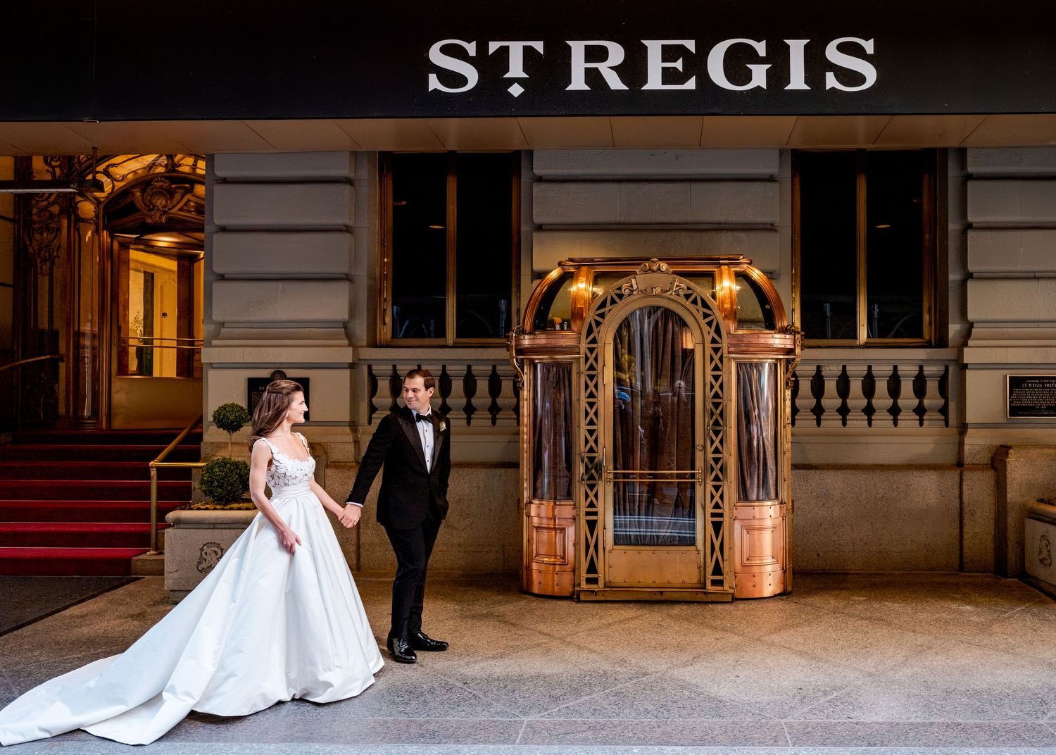 Bride and groom holding hands outside the St. Regis Hotel entrance, bride in elegant white ballgown by Oscar de la Renta.