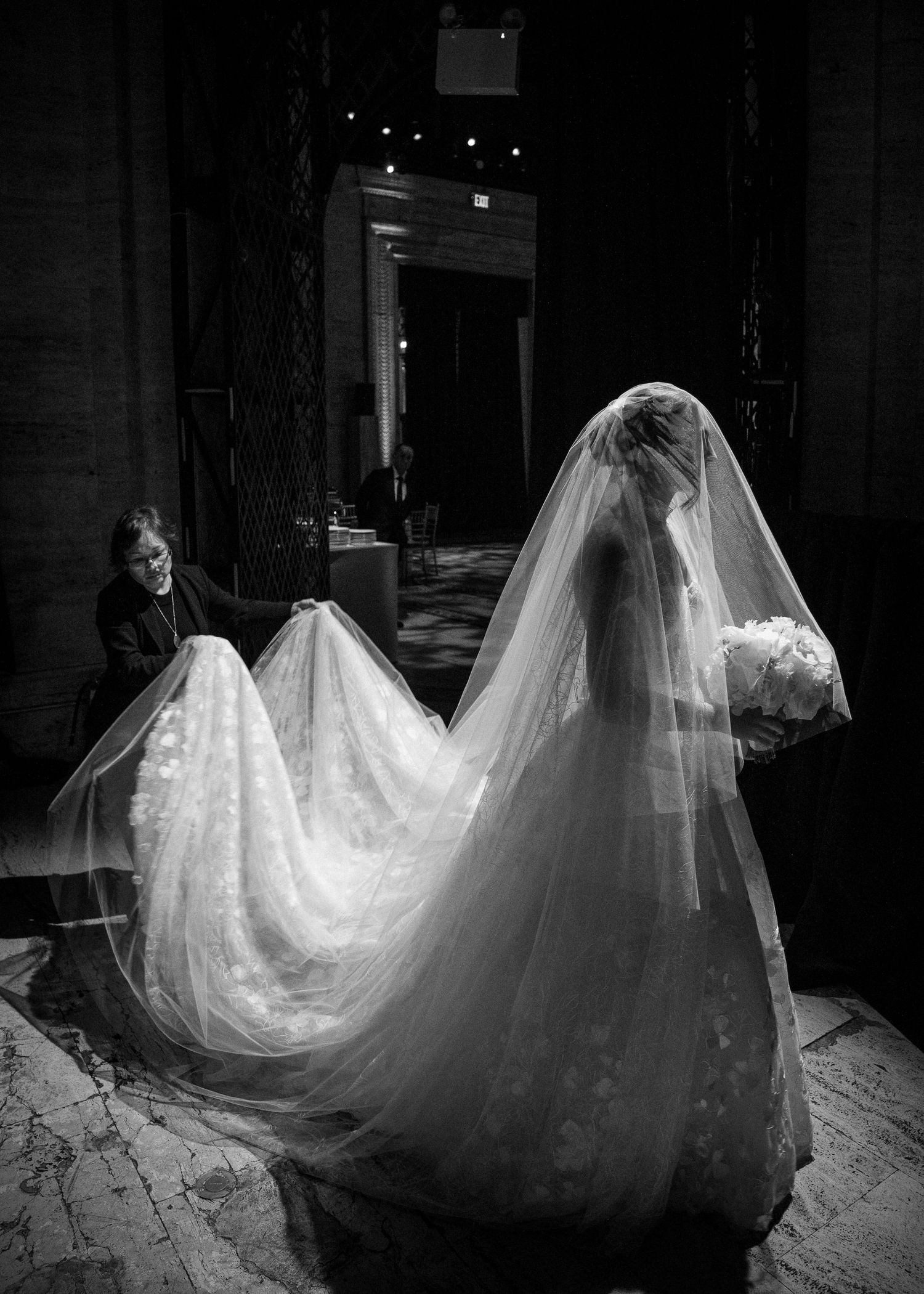 Black and white photo of a bride in a flowing lace gown and veil holding a bouquet in an elegant venue at Cipriani Wall Street, NYC.