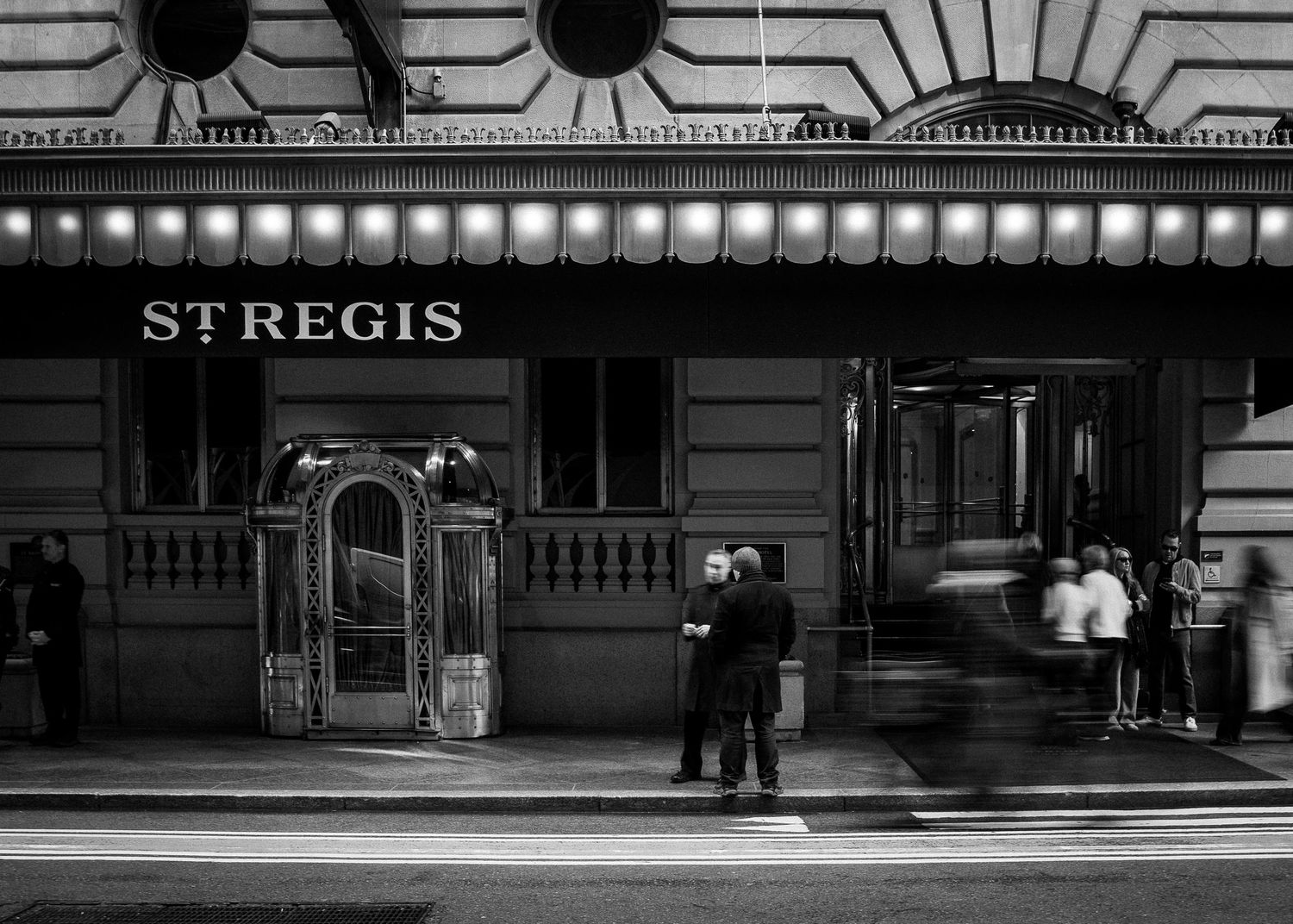 Black and white photo of couples standing outside the St. Regis hotel entrance.