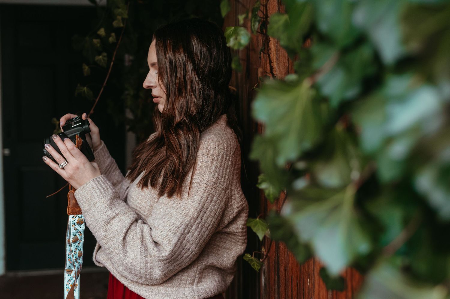 A person wearing a cozy knit sweater poses near green ivy and wooden fence.
