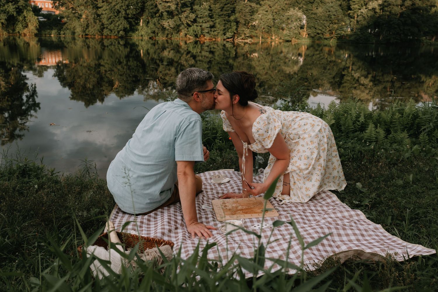 A couple relaxes on a checkered picnic blanket in a peaceful outdoor setting.