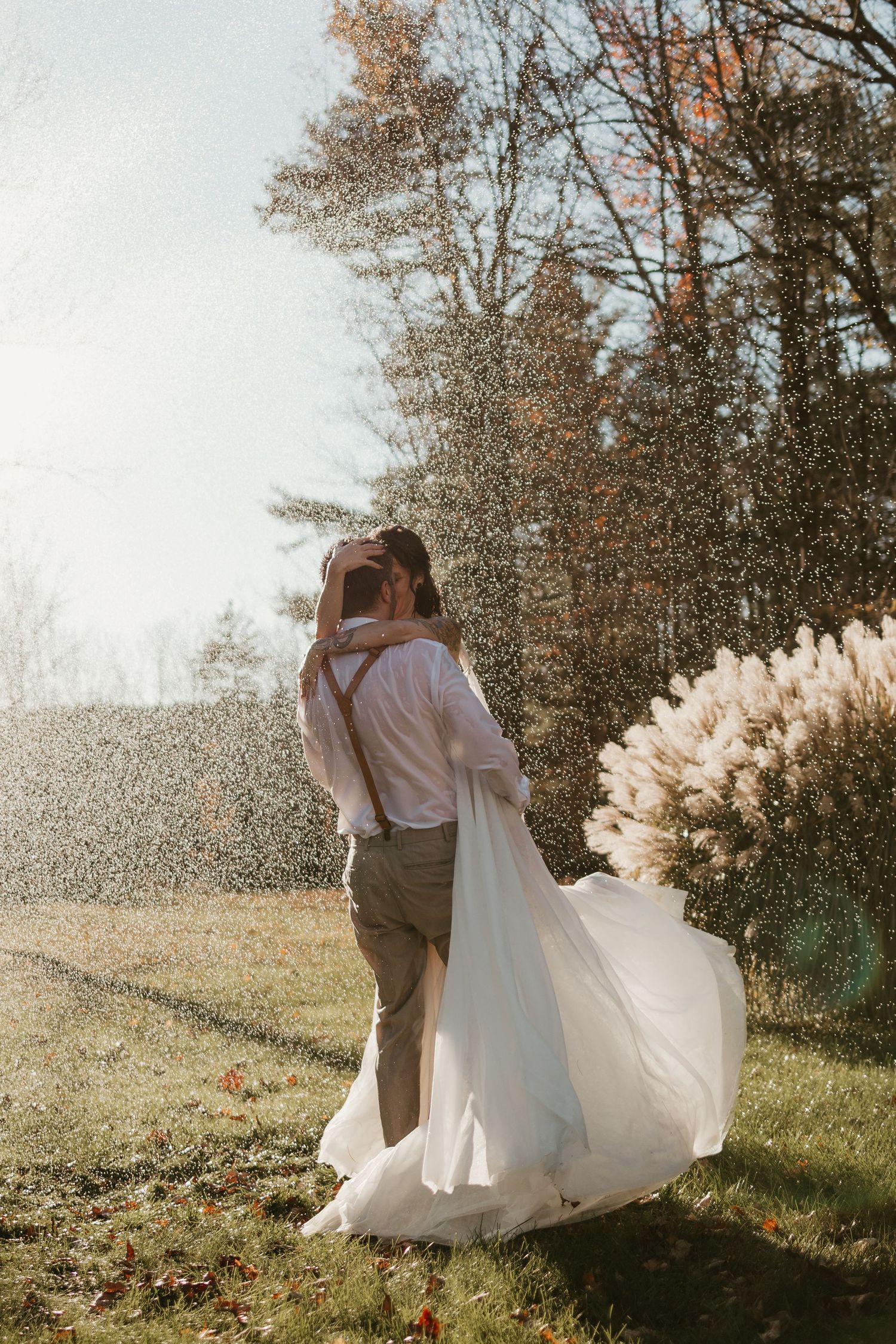 A romantic wedding couple dances in a sunlit meadow with trees in the background creating a dreamy atmosphere.