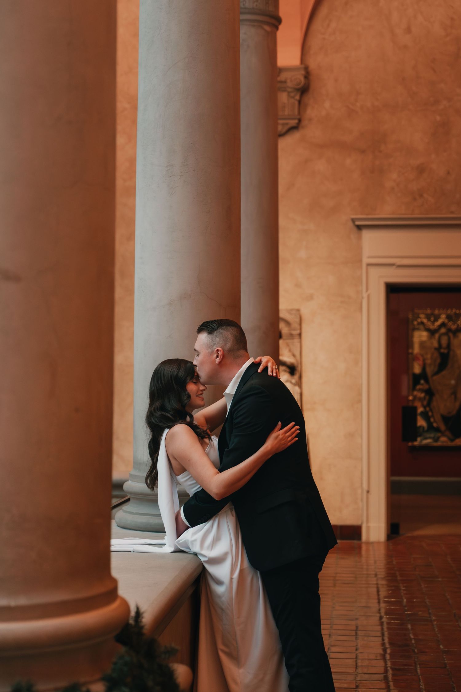 A couple shares an intimate dance moment between elegant stone columns in a historic building.