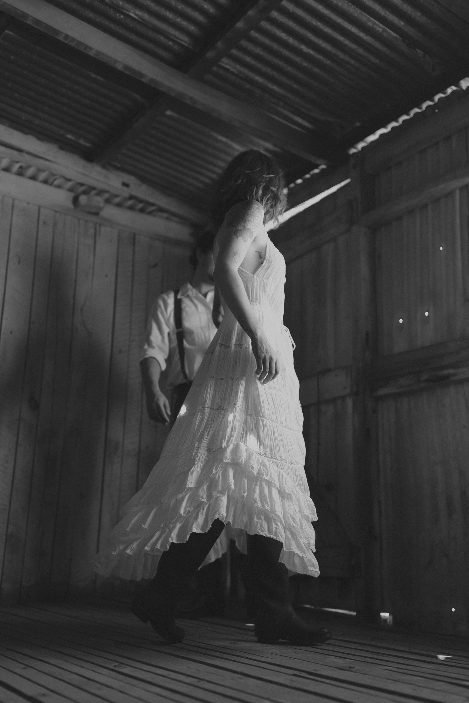 A series of dark, moody photographs showing ethereal white dresses or fabric swaying in a dimly lit wooden room.