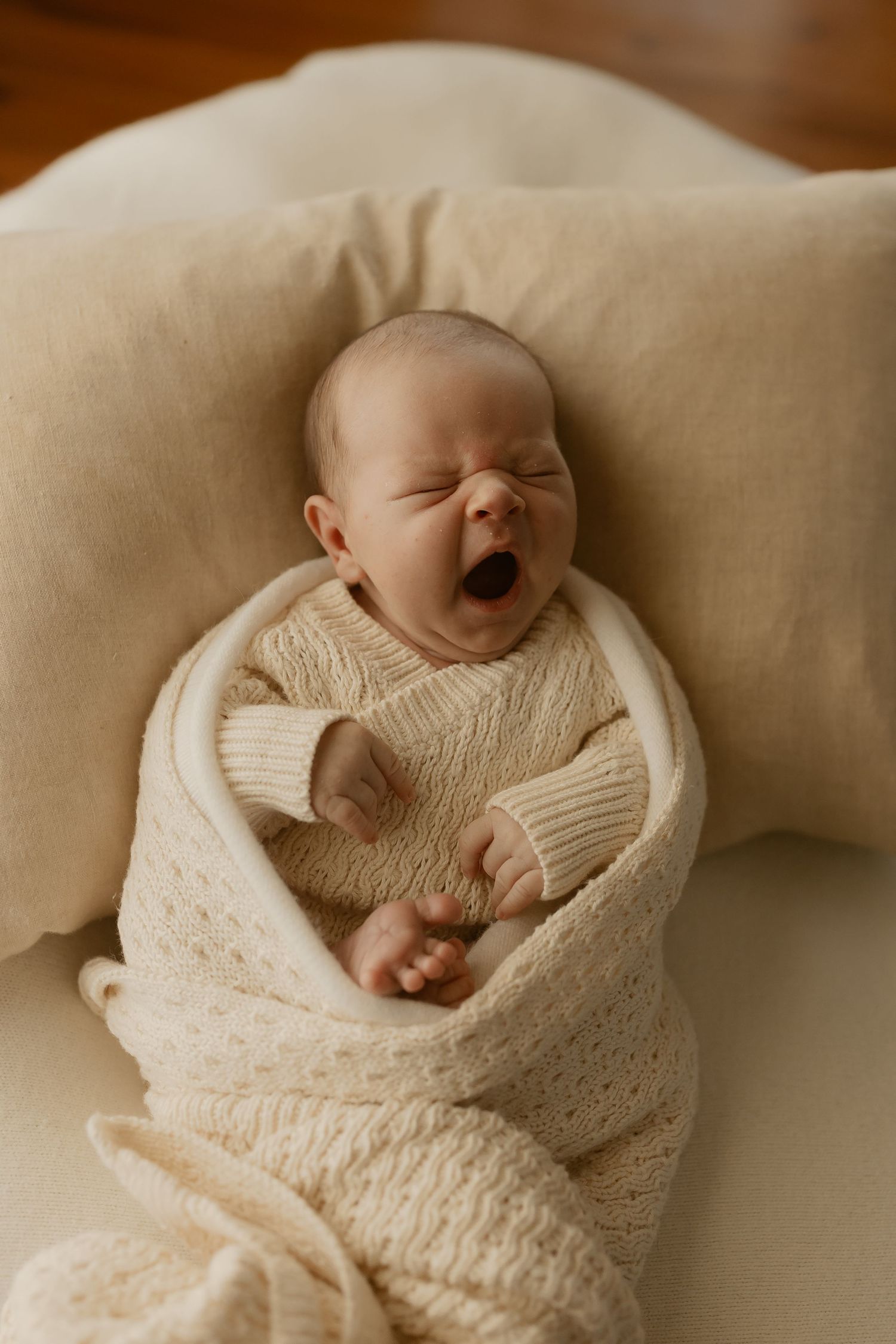 A series of lifestyle photos showing a sleeping newborn baby wrapped in a soft cream-colored blanket on beige backdrop.