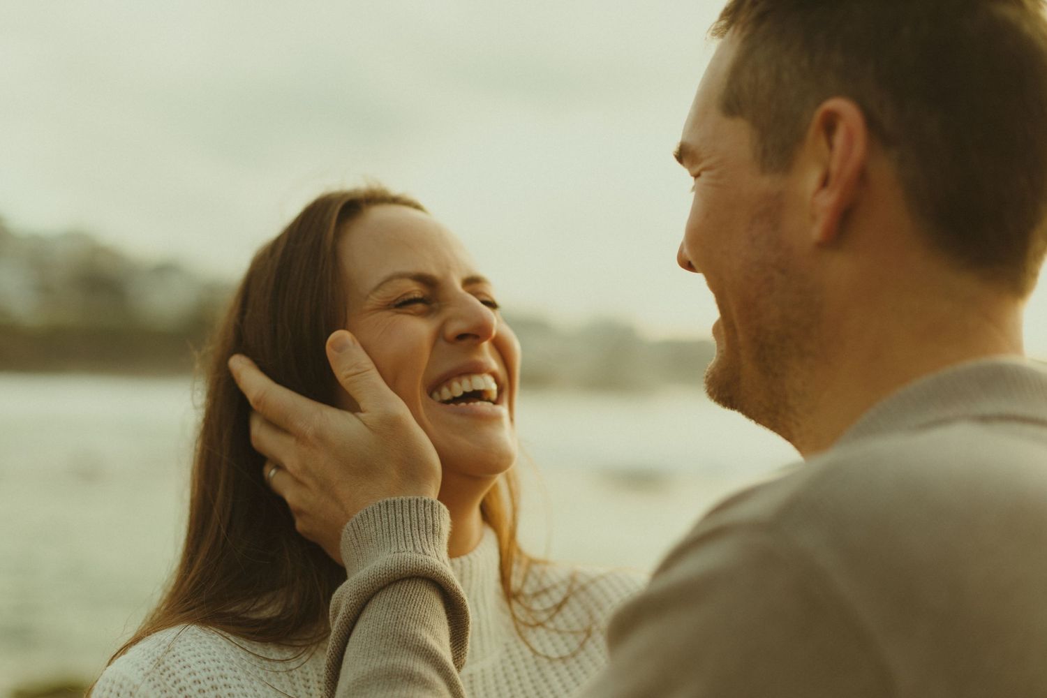 A couple laughs together while embracing during a sunset photoshoot on the beach.