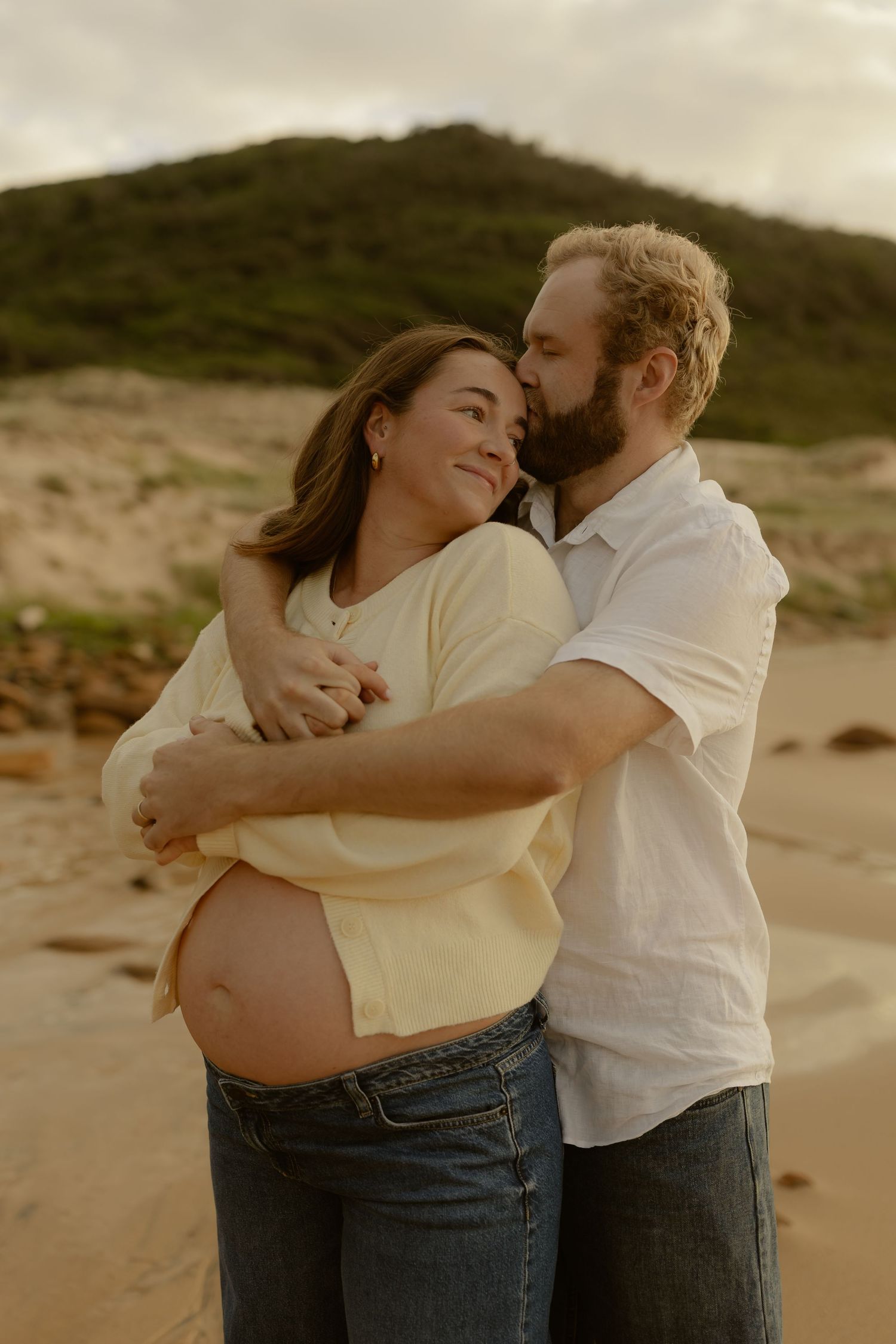 Romantic couple embraces on a sandy beach during golden hour, creating intimate silhouettes against nature.