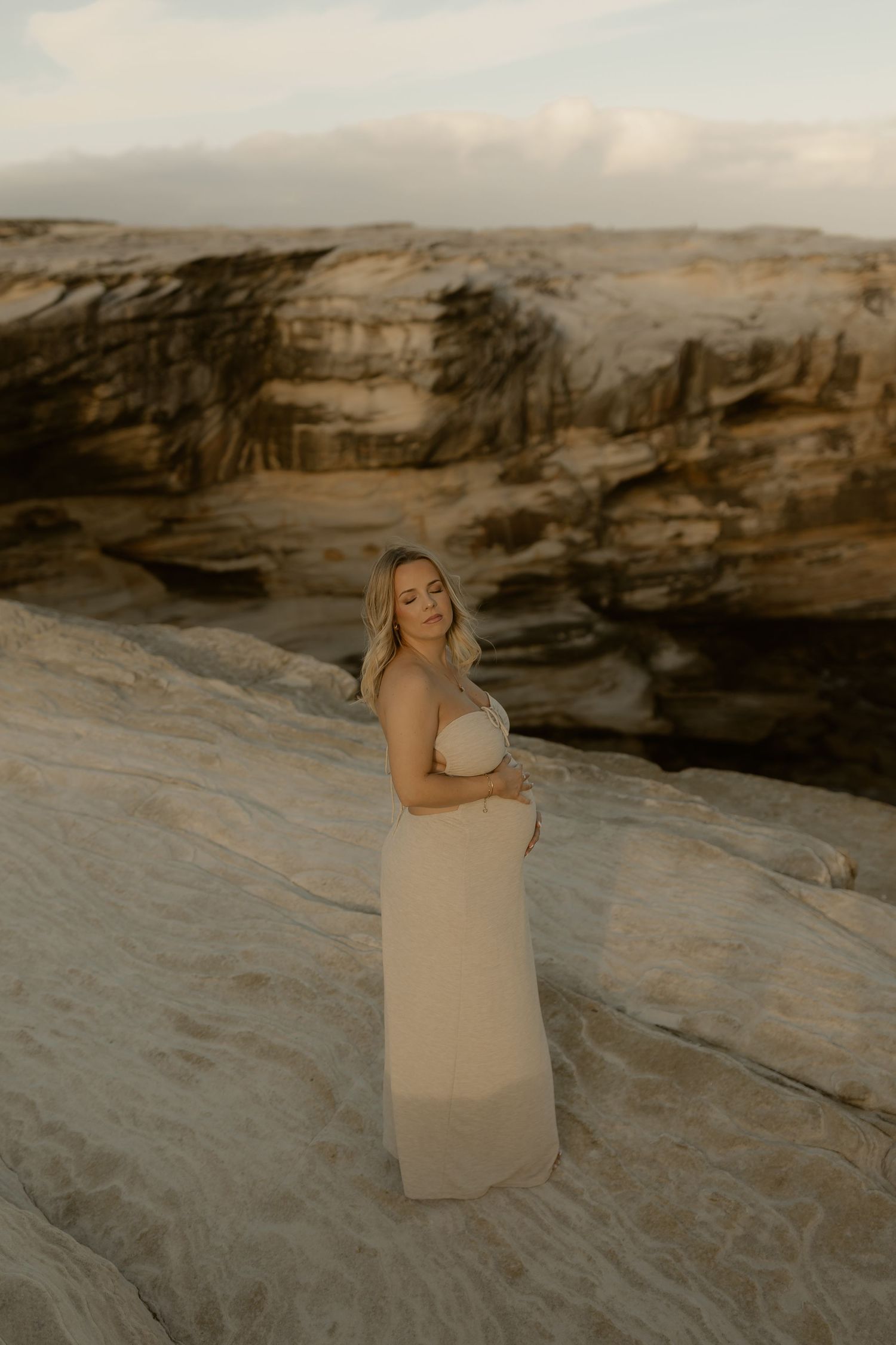Person in beige dress poses on textured rock formations during golden hour photography session.