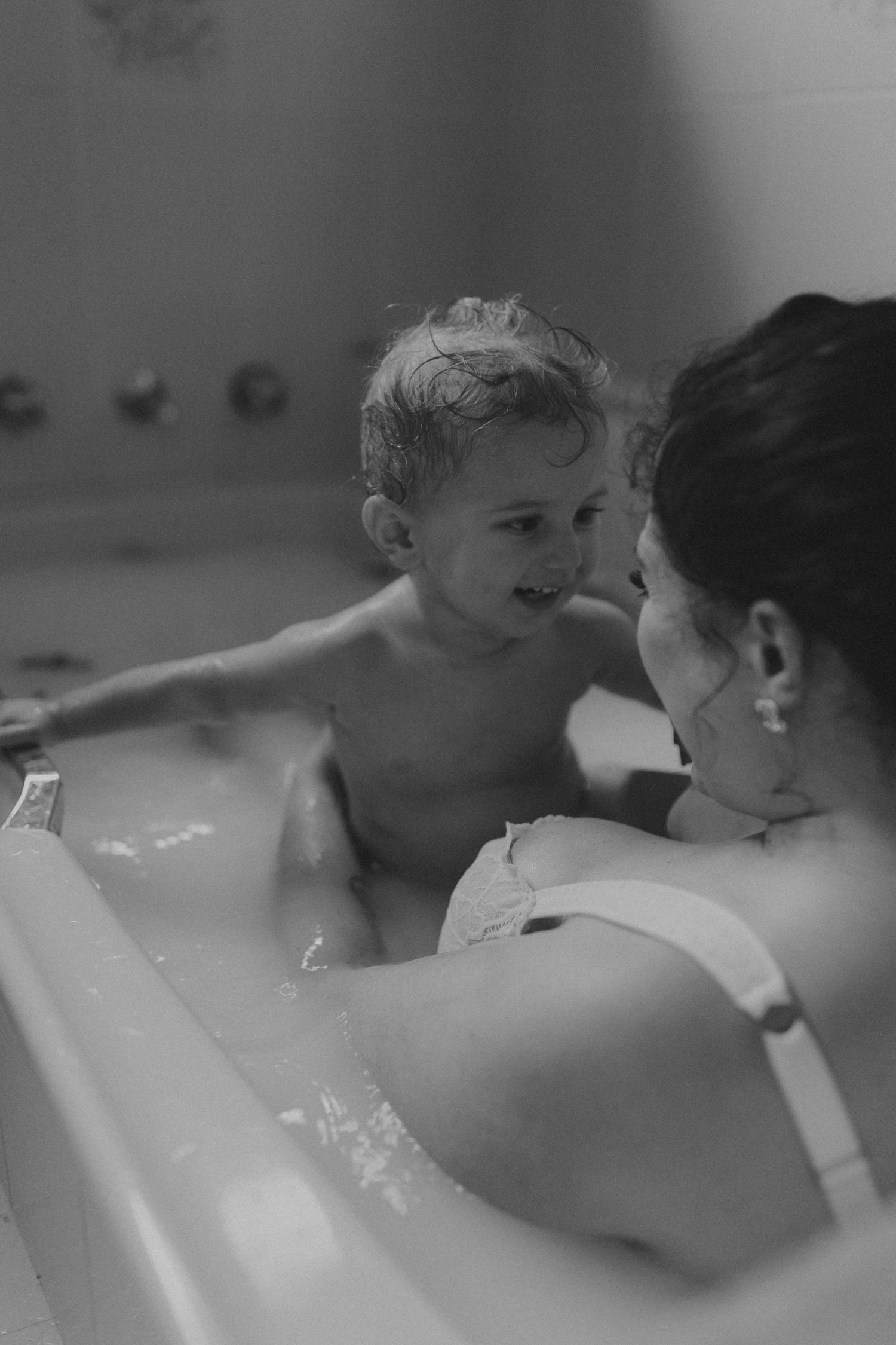 Black and white photograph of playful bathtime interaction between parent and child.
