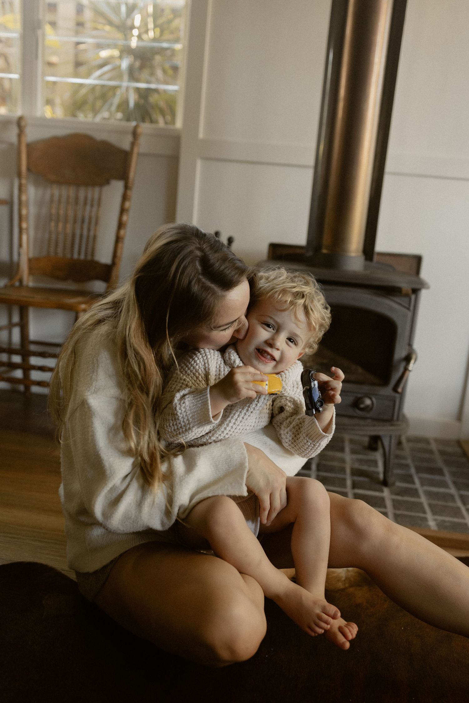 Candid moment by a wood stove showing shared joy and connection in cream sweaters.
