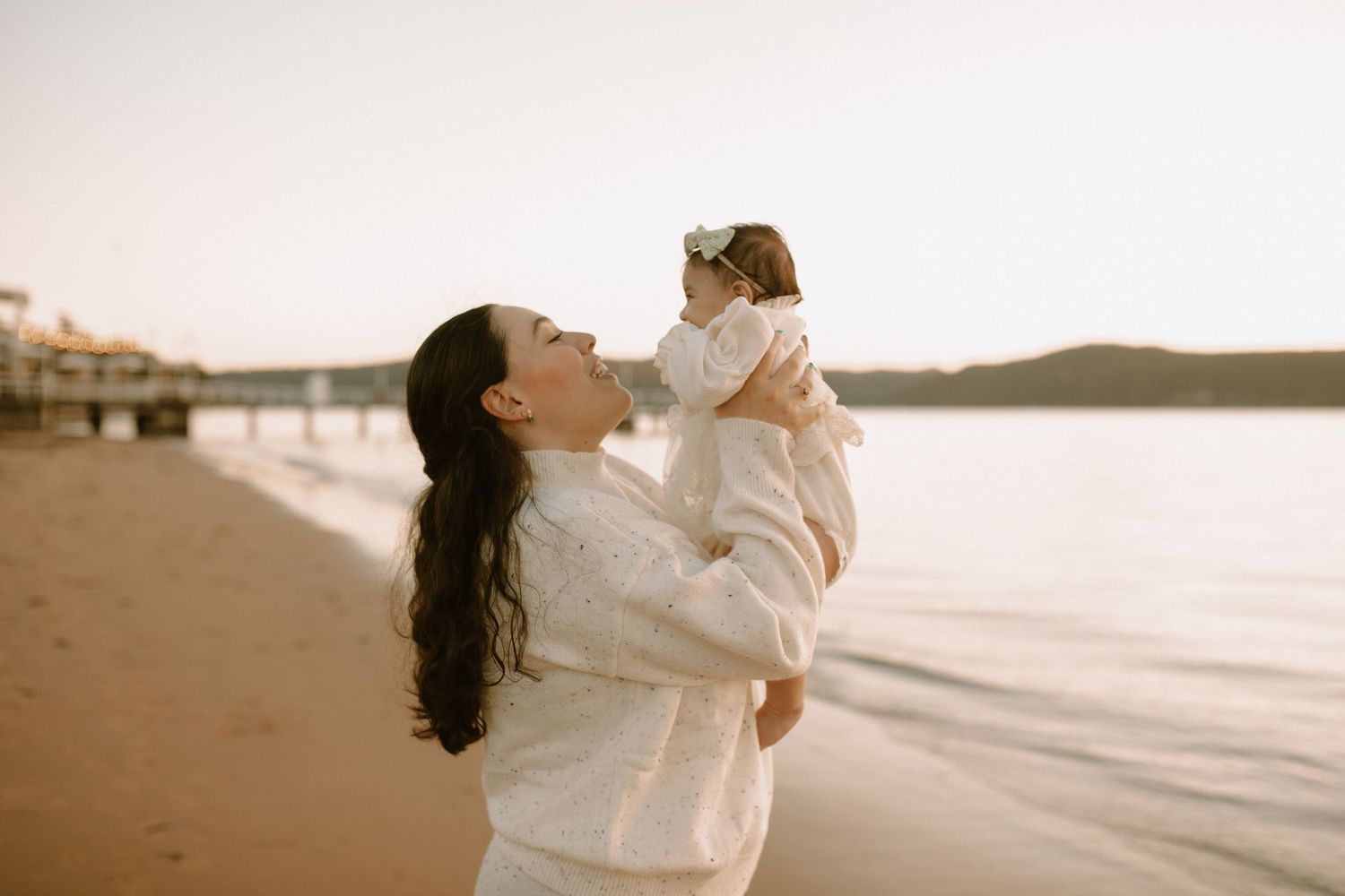 Parent and child in white outfits playing together on a golden sunset beach.