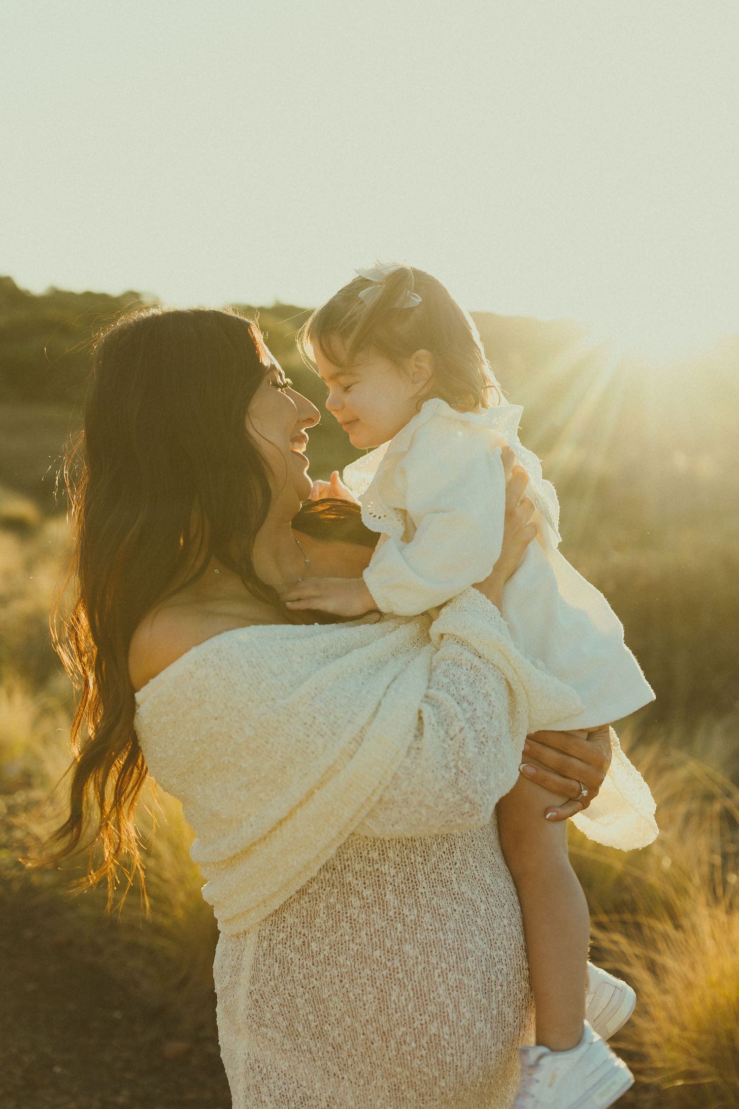 A tender moment between parent and child embracing in golden sunlight with tall grass and mountains in background.