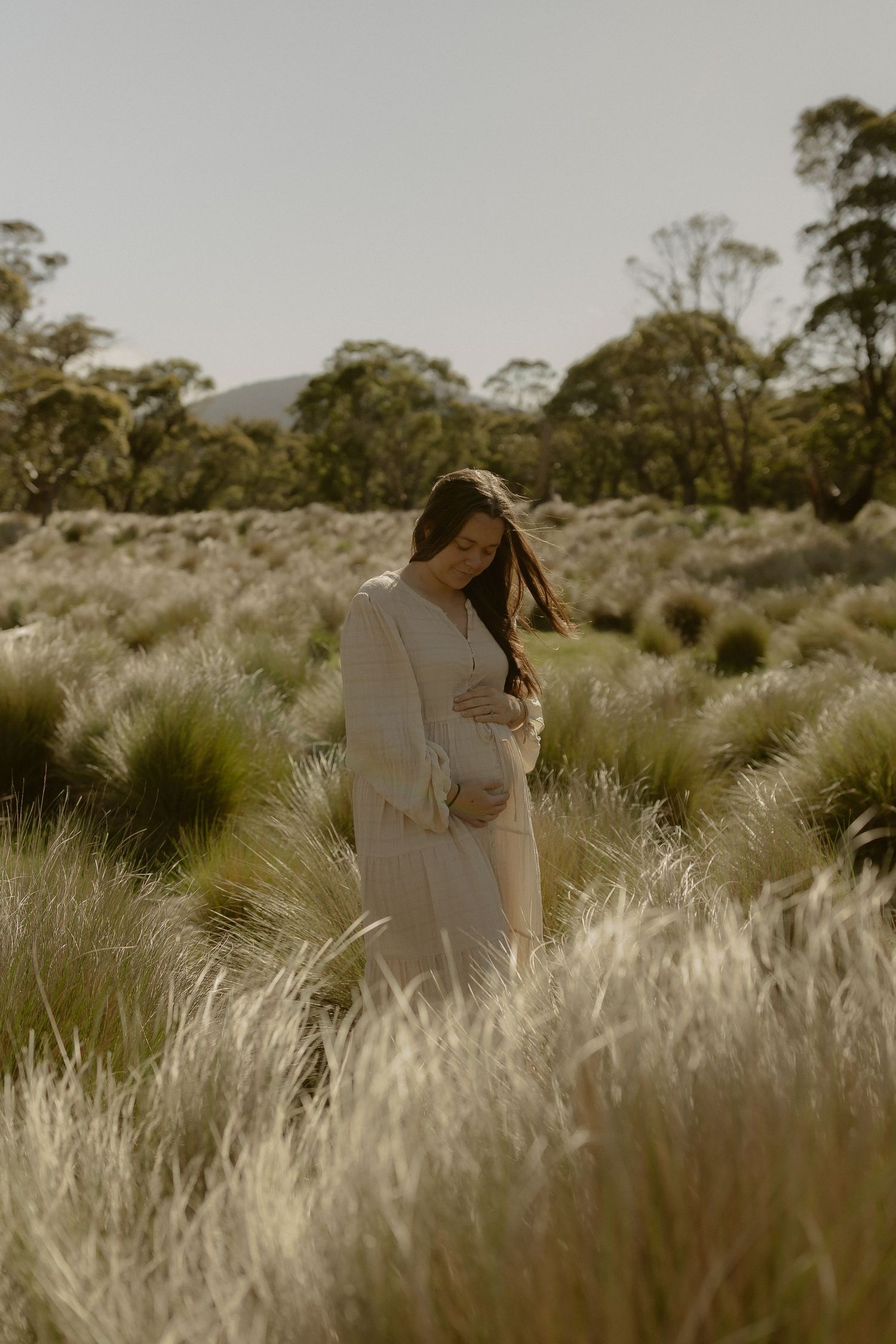 A couple embraces tenderly in a golden field of tall grass at sunset creating a romantic silhouette.