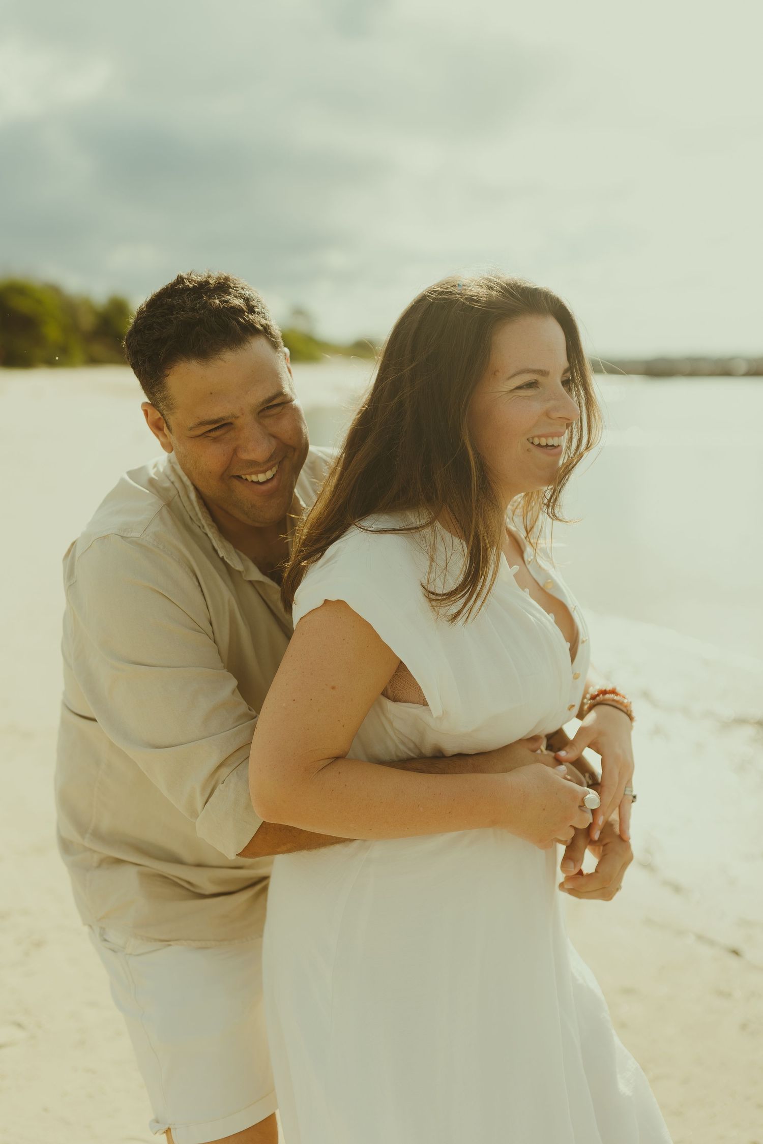 Couple laughing and embracing while enjoying a romantic moment on a sunny beach.