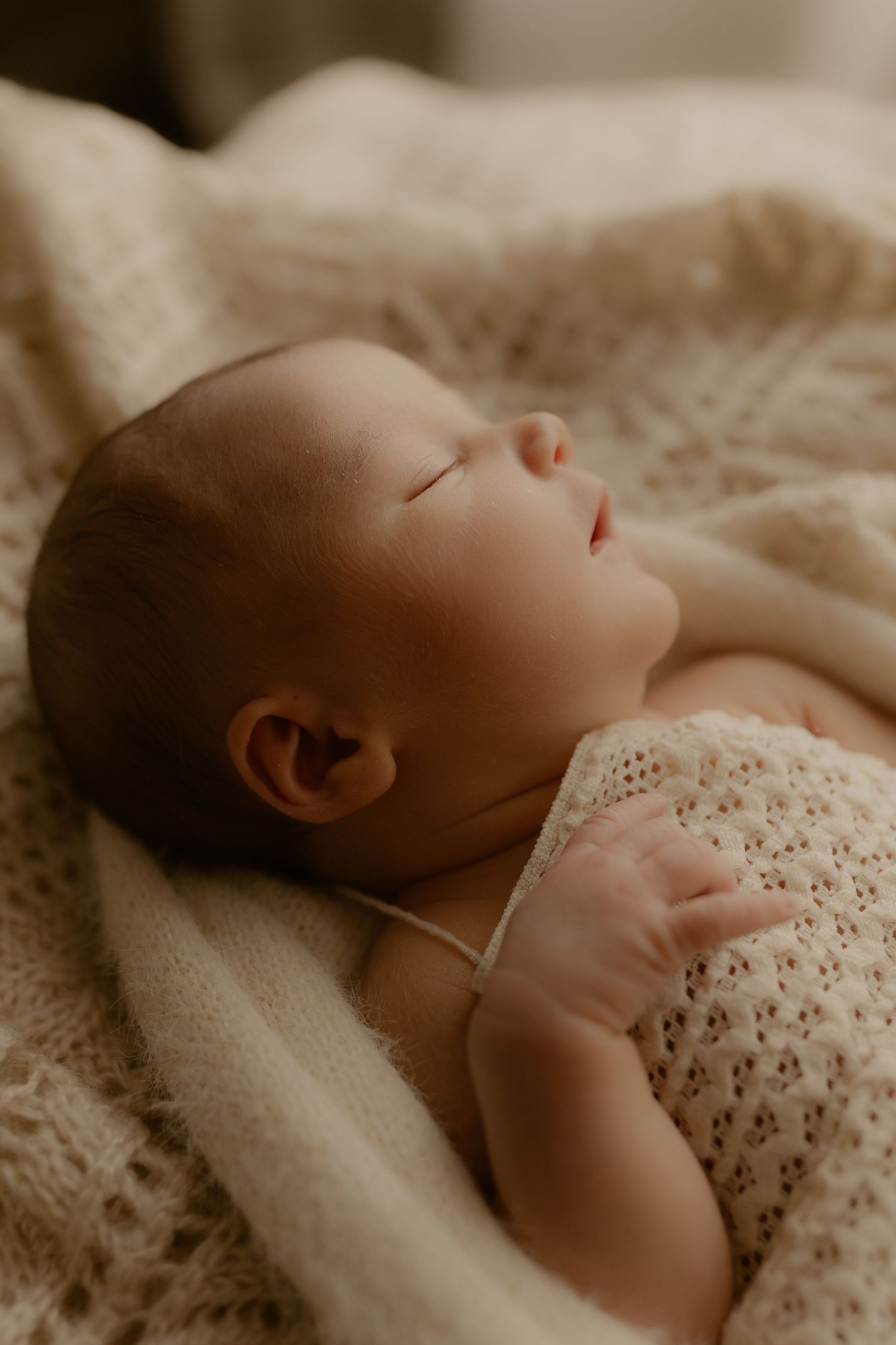 Newborn baby sleeping peacefully on soft white textured blanket in sepia tones.