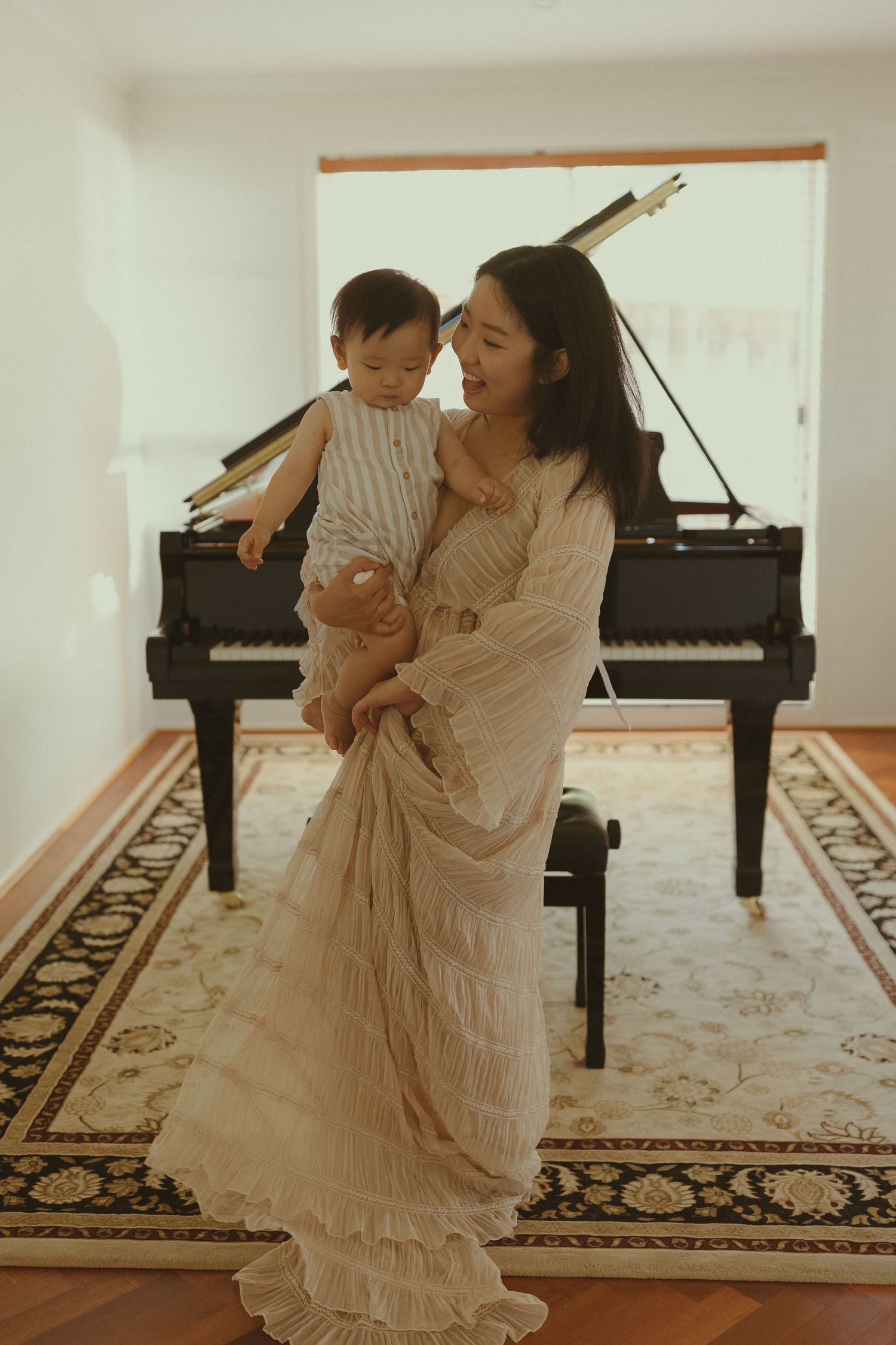 A flowing white dress creates an elegant silhouette against a grand piano in a sunlit room.