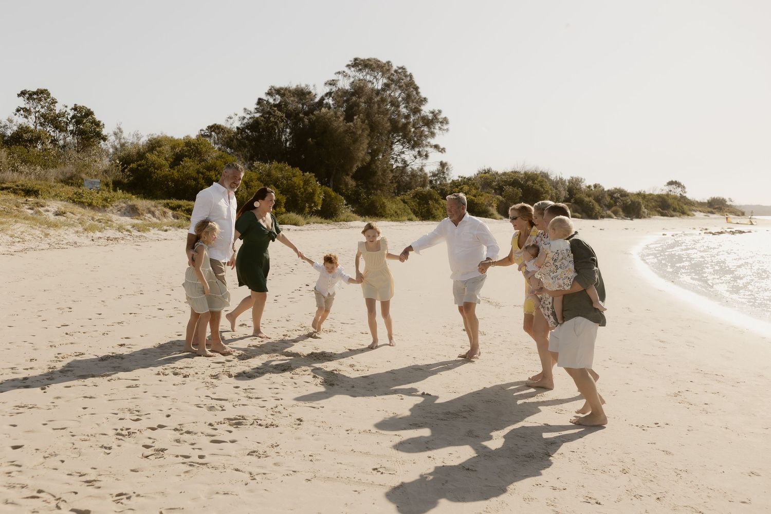 People gathered in a circle playing a game on a sunny beach with trees in the background.