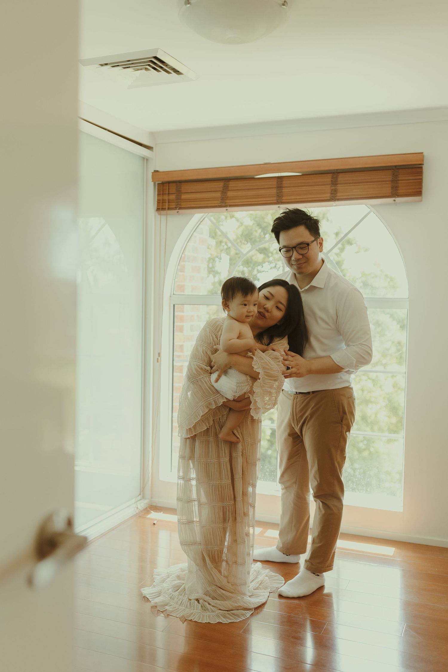 A family shares a tender moment in a sunlit room with wooden floors.
