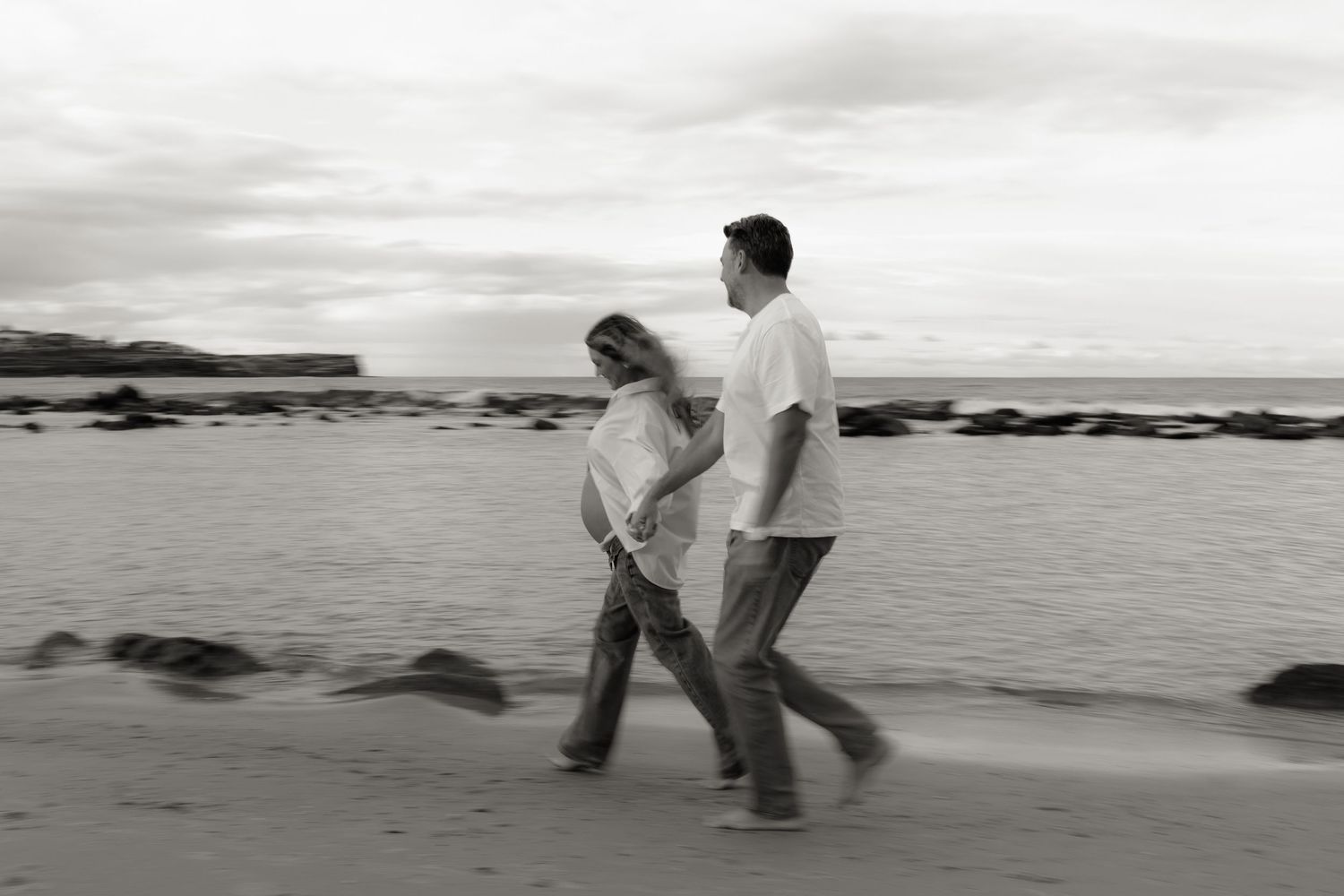Black and white photo of a couple walking hand in hand along a rocky beach.