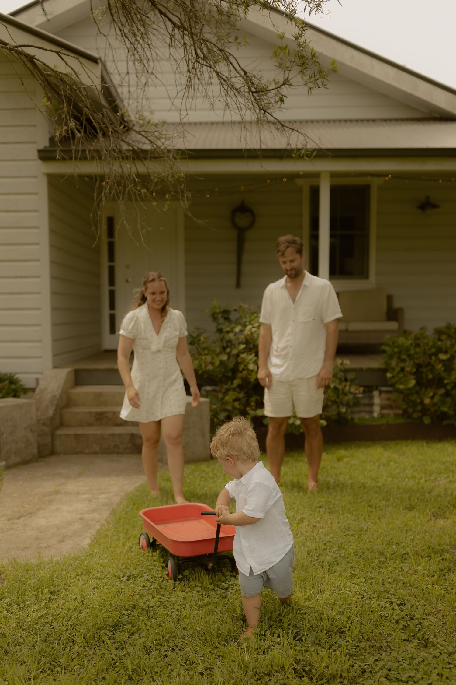 A summer scene shows a red wagon being pulled across a lawn in front of a white farmhouse.