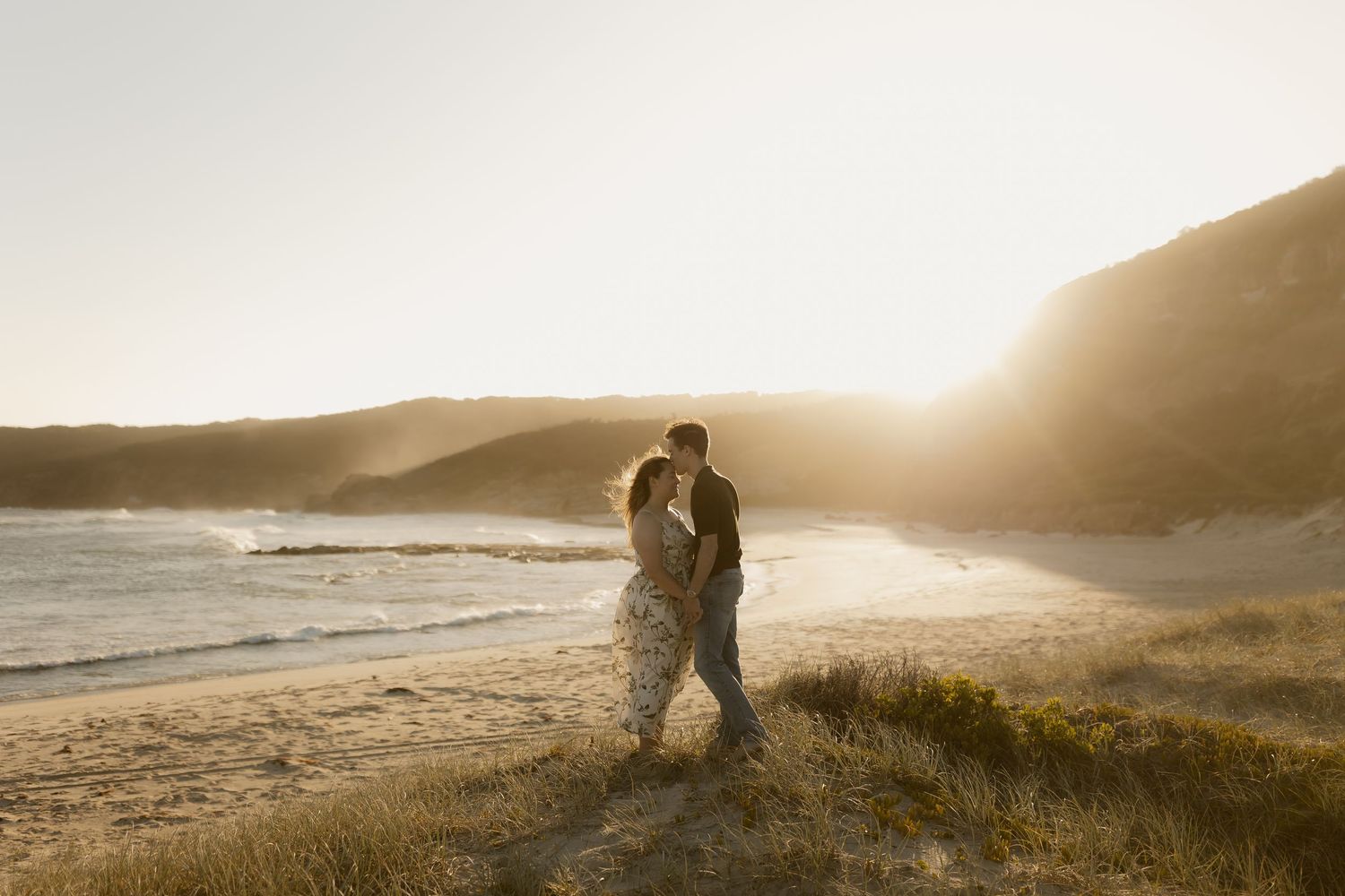 Panoramic view of a beach at sunset with silhouettes walking along the shoreline.