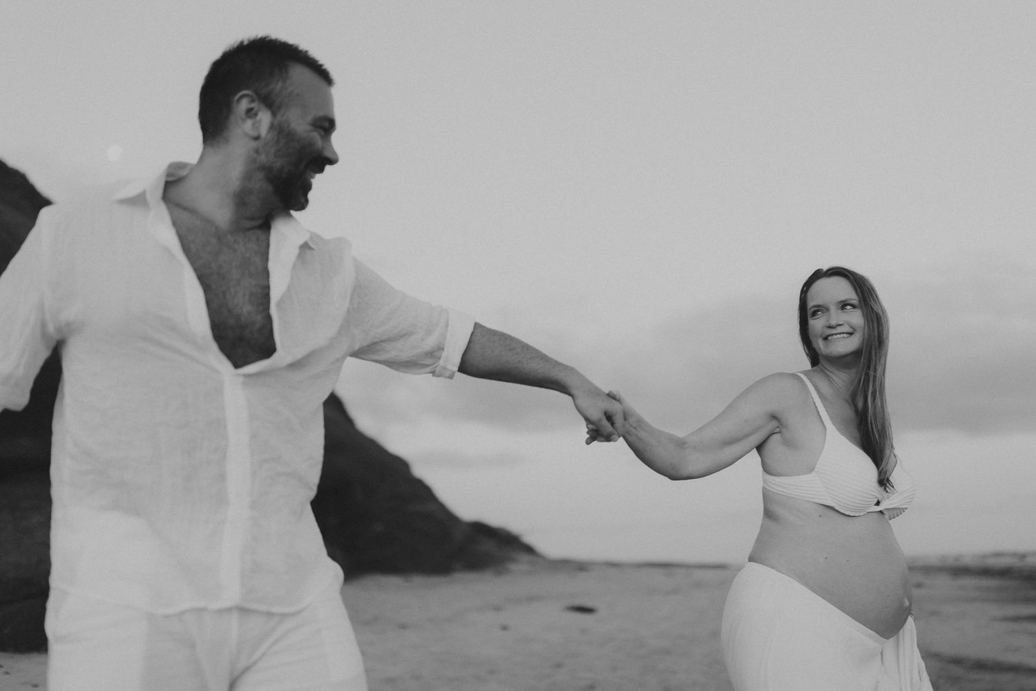 A couple laughs and embraces while enjoying a romantic moment on the beach.