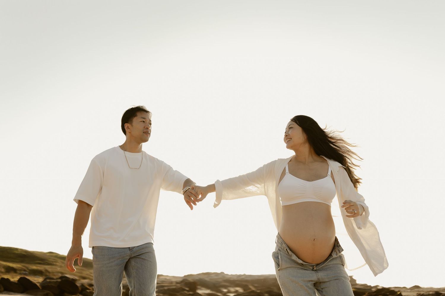 Couple holding hands and walking together on coastal cliffs during sunset.