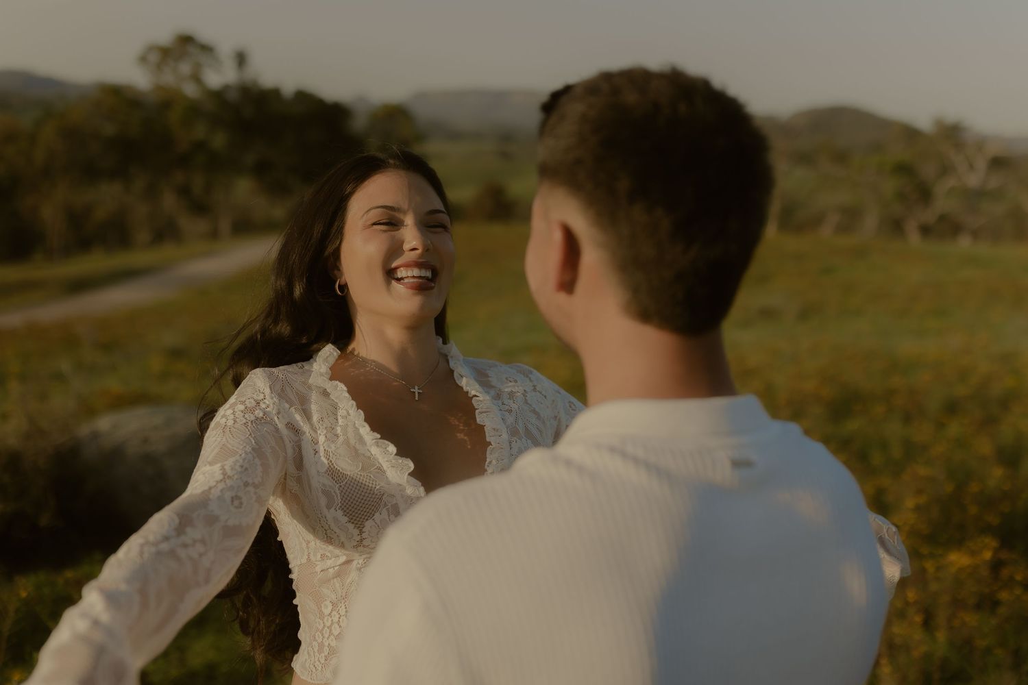 A couple shares a joyful moment together in a scenic countryside setting during golden hour.