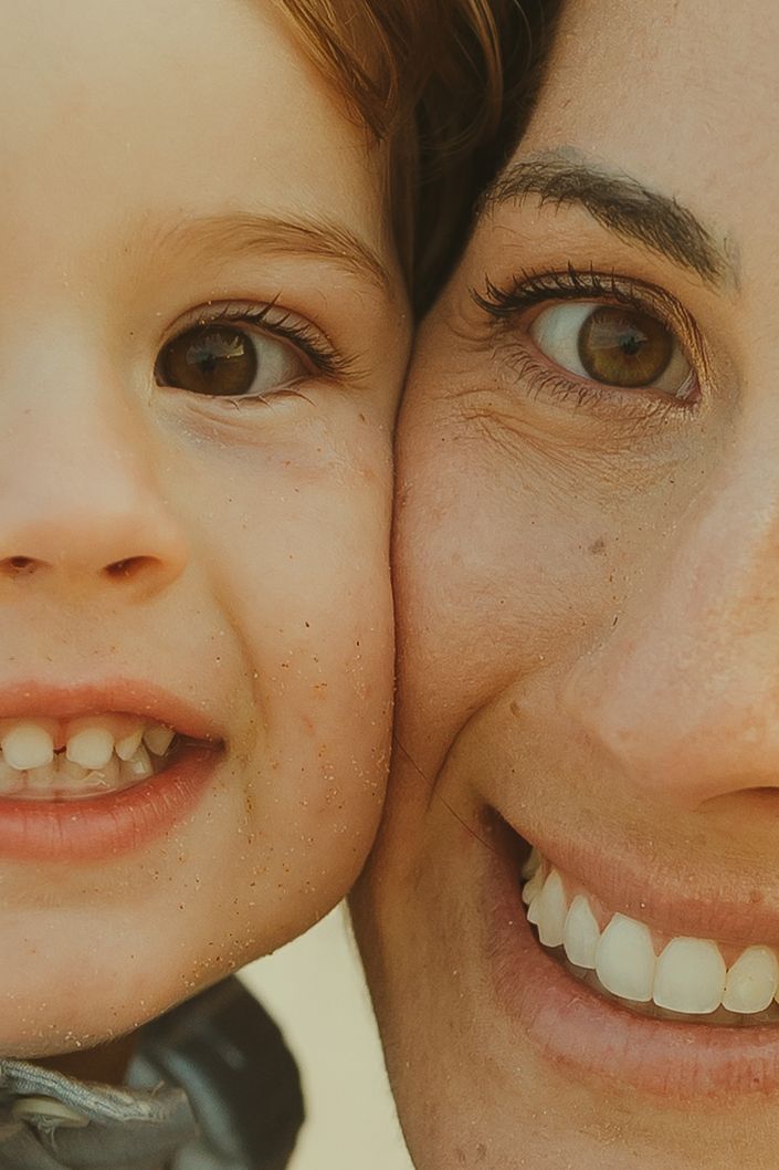 Close-up portrait of two smiling faces with brown eyes pressed together showing joyful expressions.