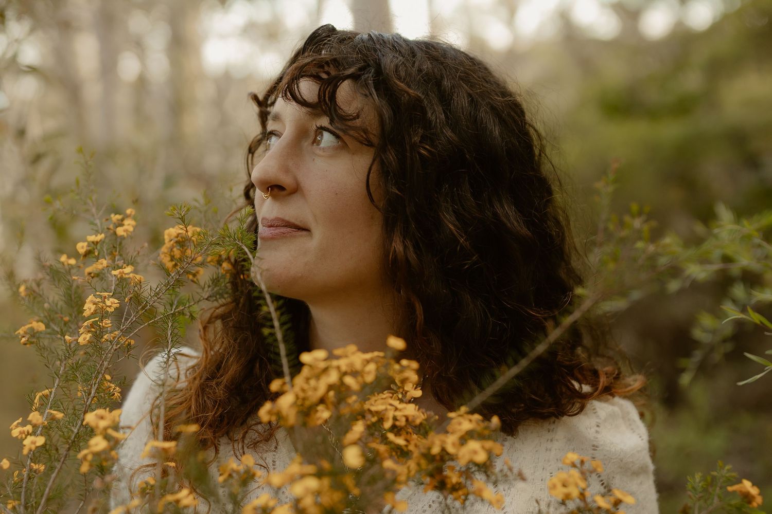 A woman in white stands among yellow wildflowers in a natural outdoor setting.