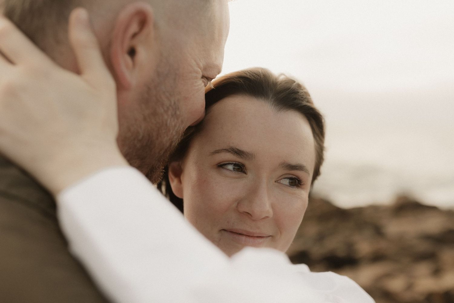 A tender moment between a couple captured in soft natural light against a rocky outdoor backdrop.