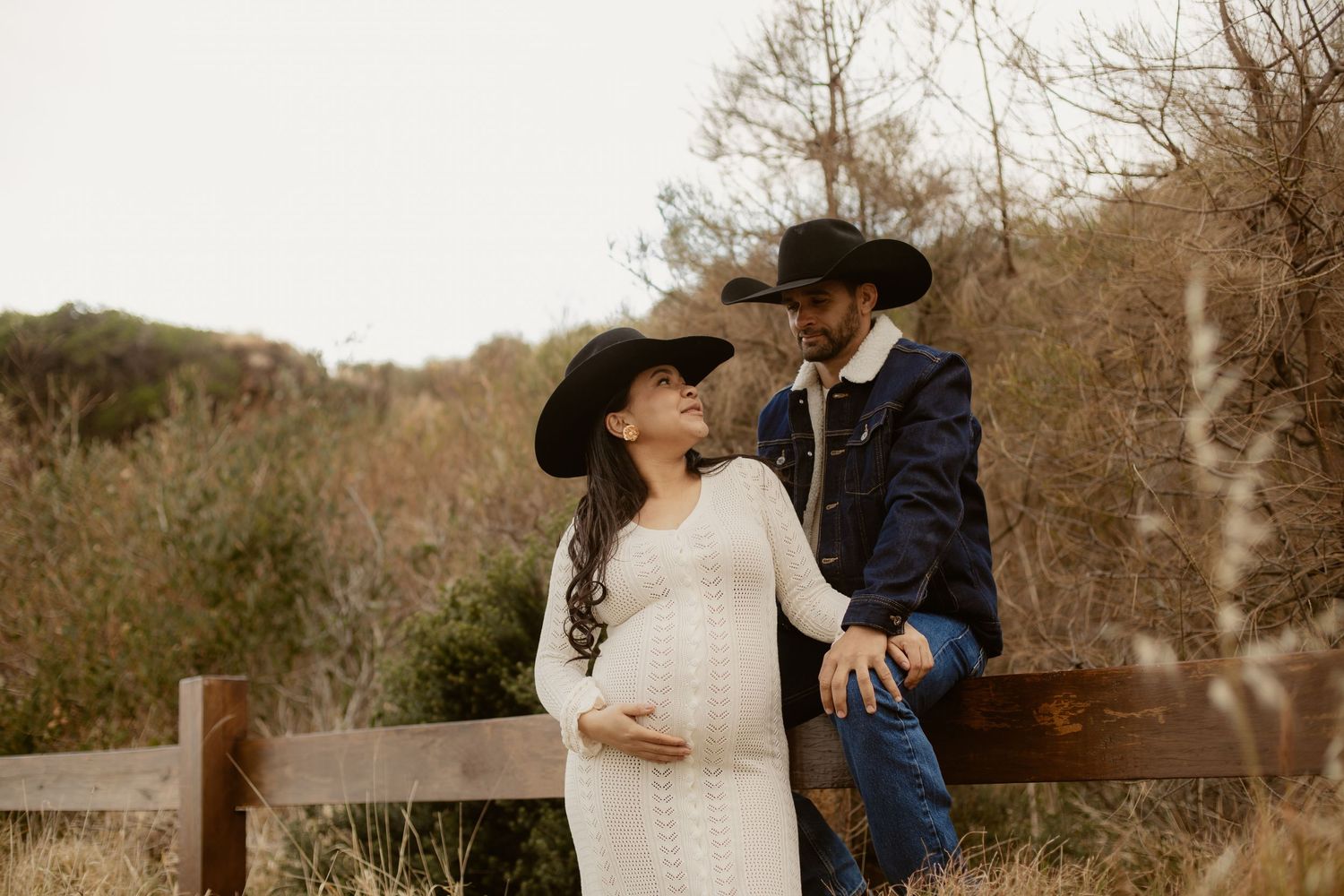 A romantic couple shares tender moments in a rustic outdoor setting with trees and natural scenery in the background.