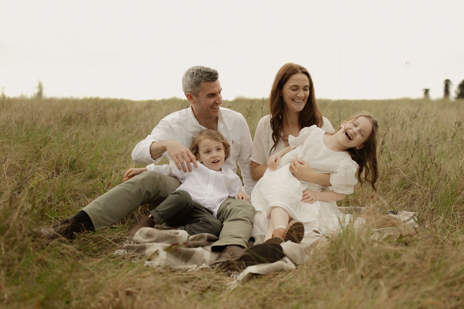 A family sits together on a blanket in a grassy field during a warm afternoon photo session.