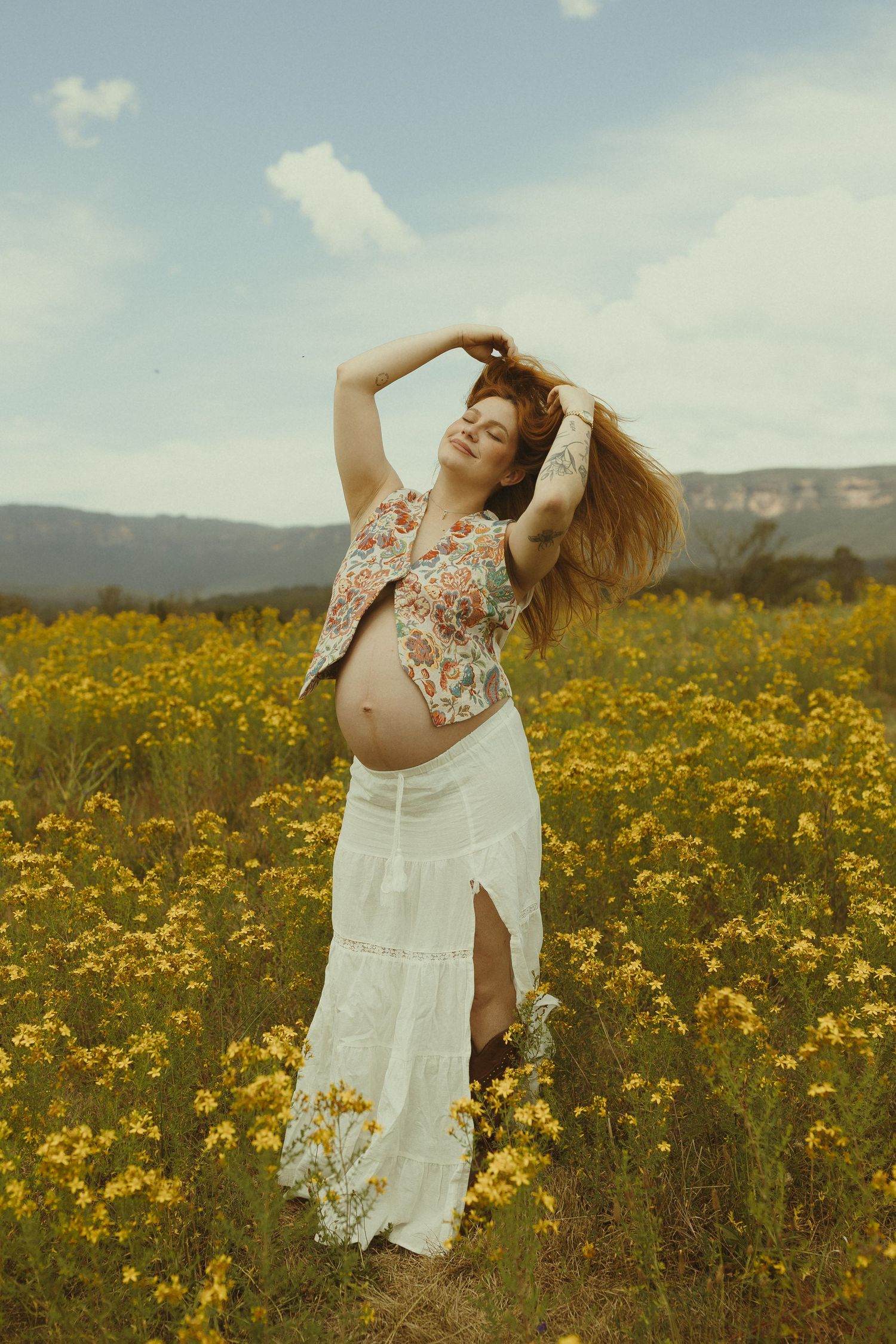 A white dress flows in the breeze as someone dances joyfully among yellow wildflowers under blue skies.