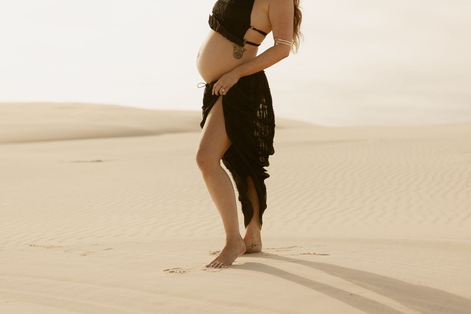 Intimate desert photography session with a horse and couple among rolling sand dunes in warm light.