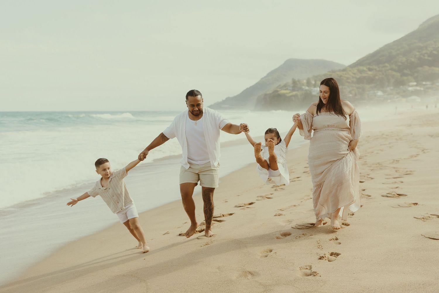 People walking together and leaving footprints on a sandy beach with mountains in the background.