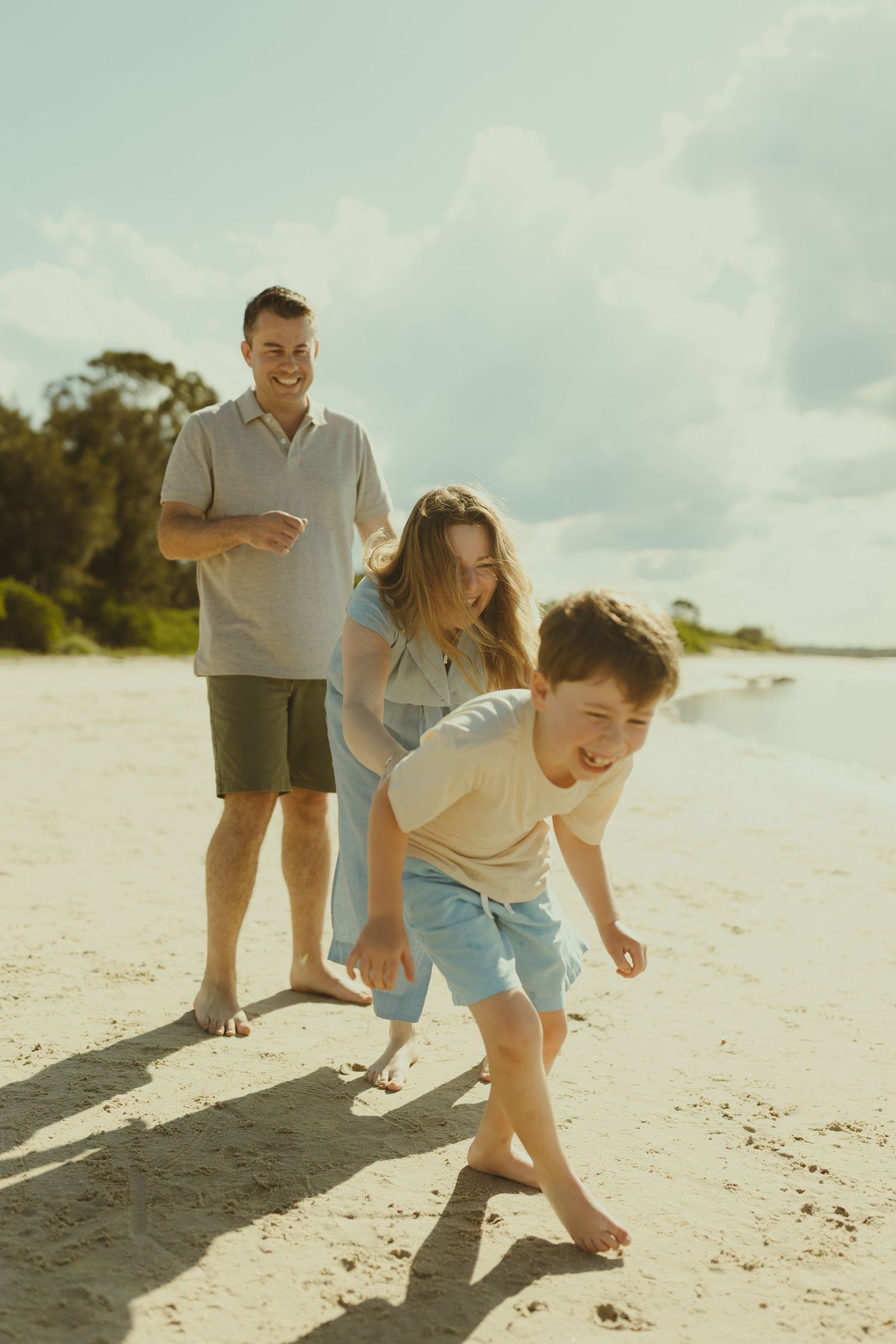 Family members playing and running together on a white sandy beach.